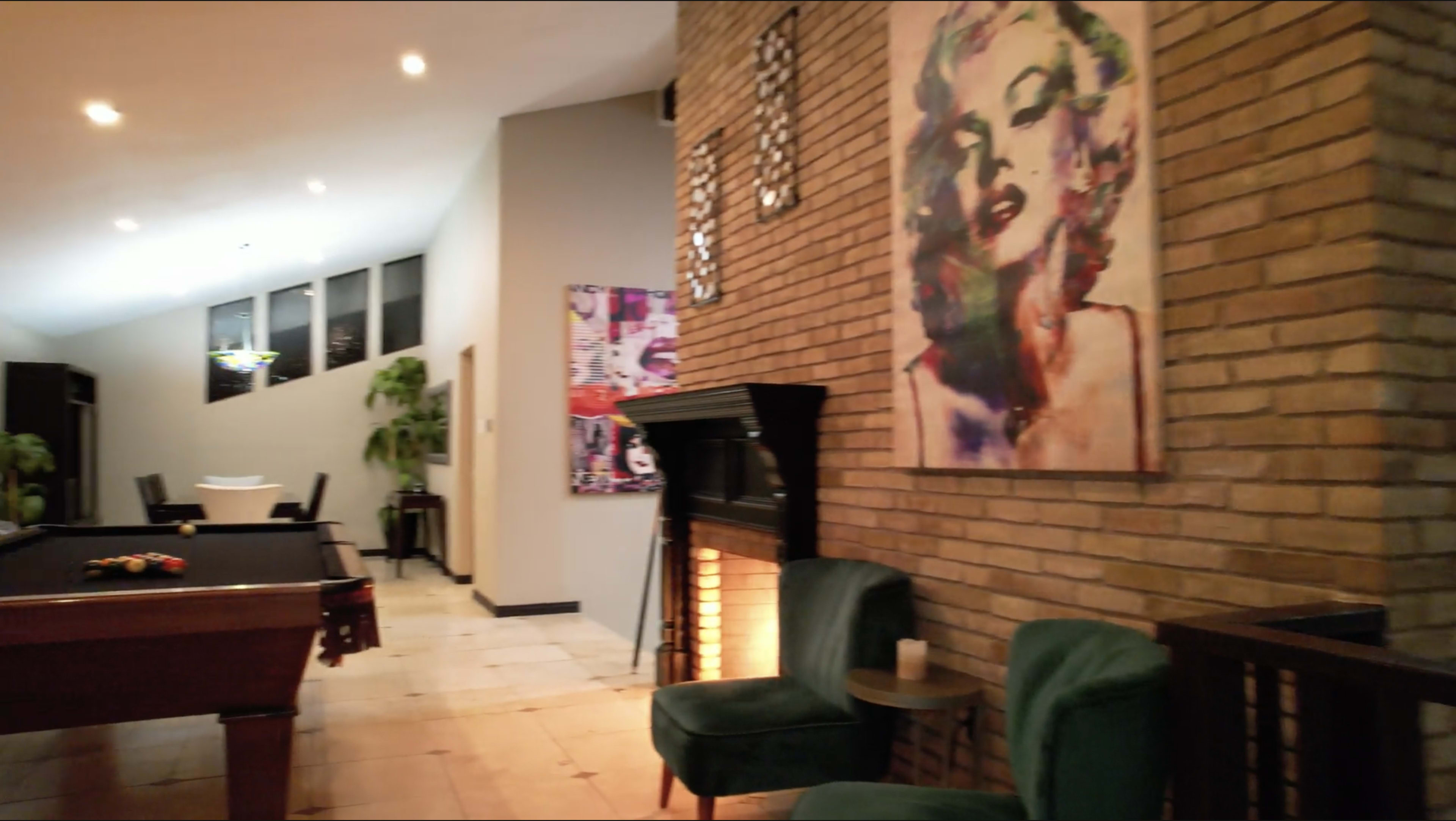 A spacious indoor area with a pool table, a fireplace, and a colorful portrait on the brick wall, complemented by green chairs.