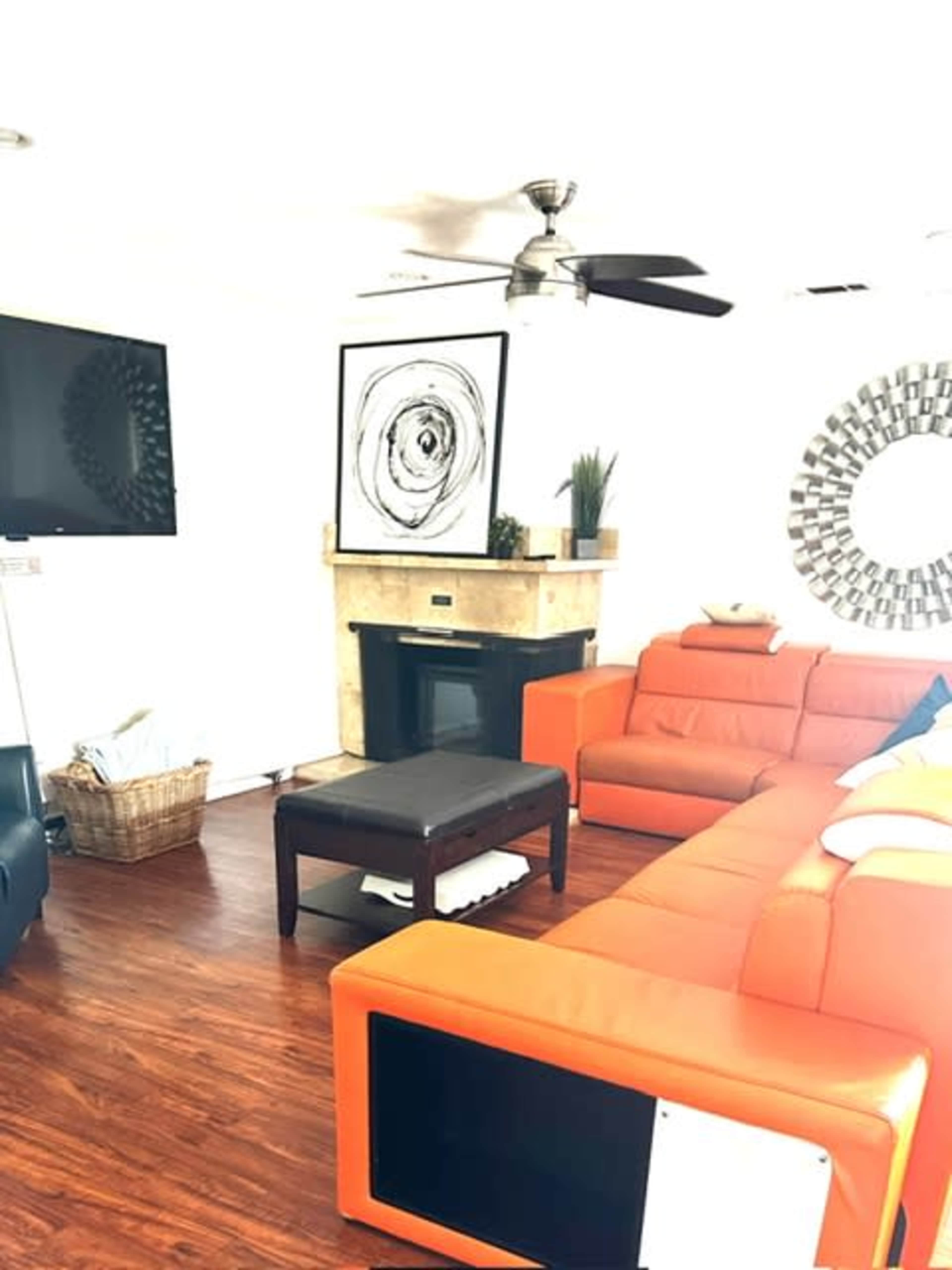 The living room features an orange sectional sofa, a black coffee table, a fireplace with a stone mantel, and a wall-mounted television.