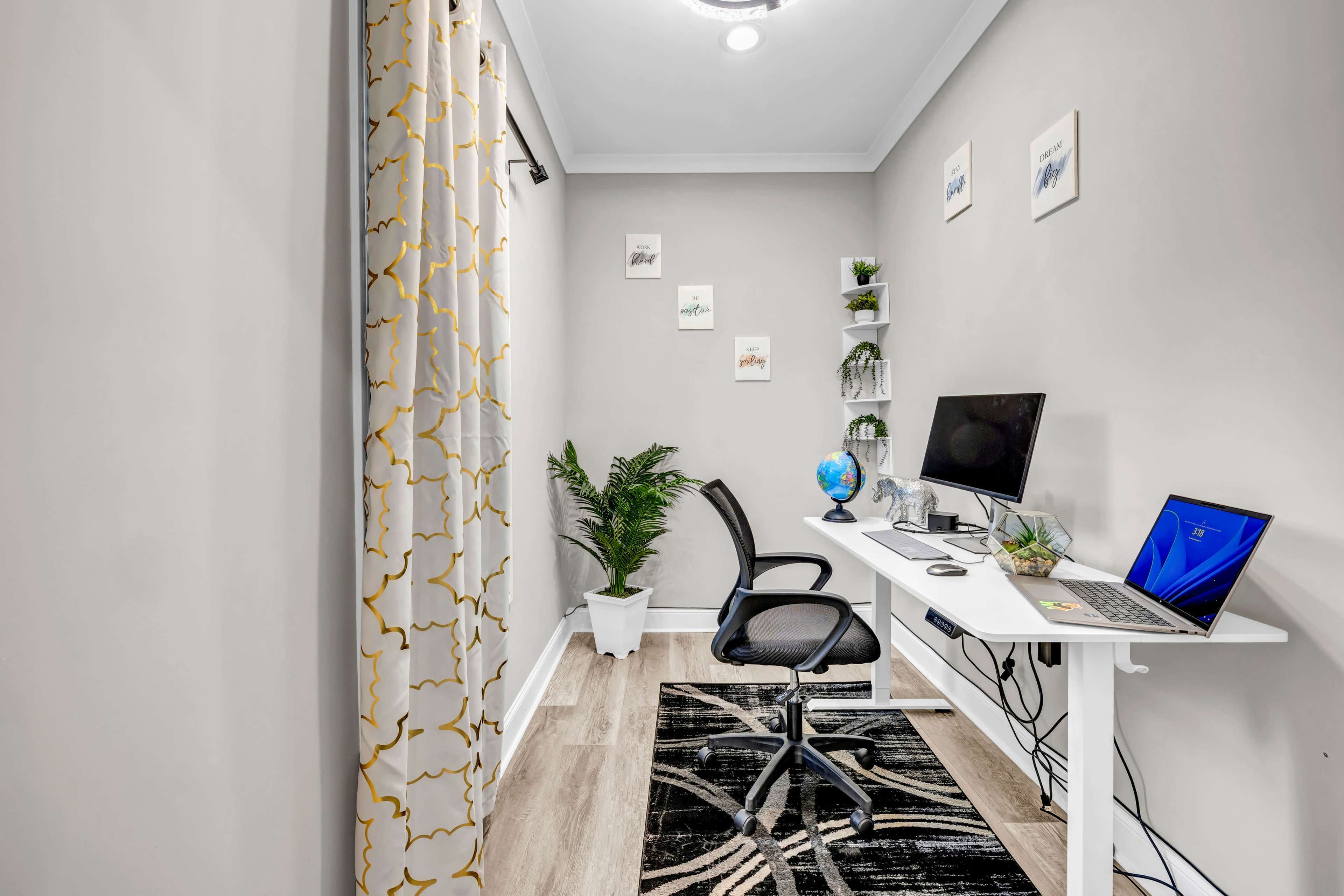 The image shows a modern home office with a desk, computer, chair, plants, and decorative wall art.
