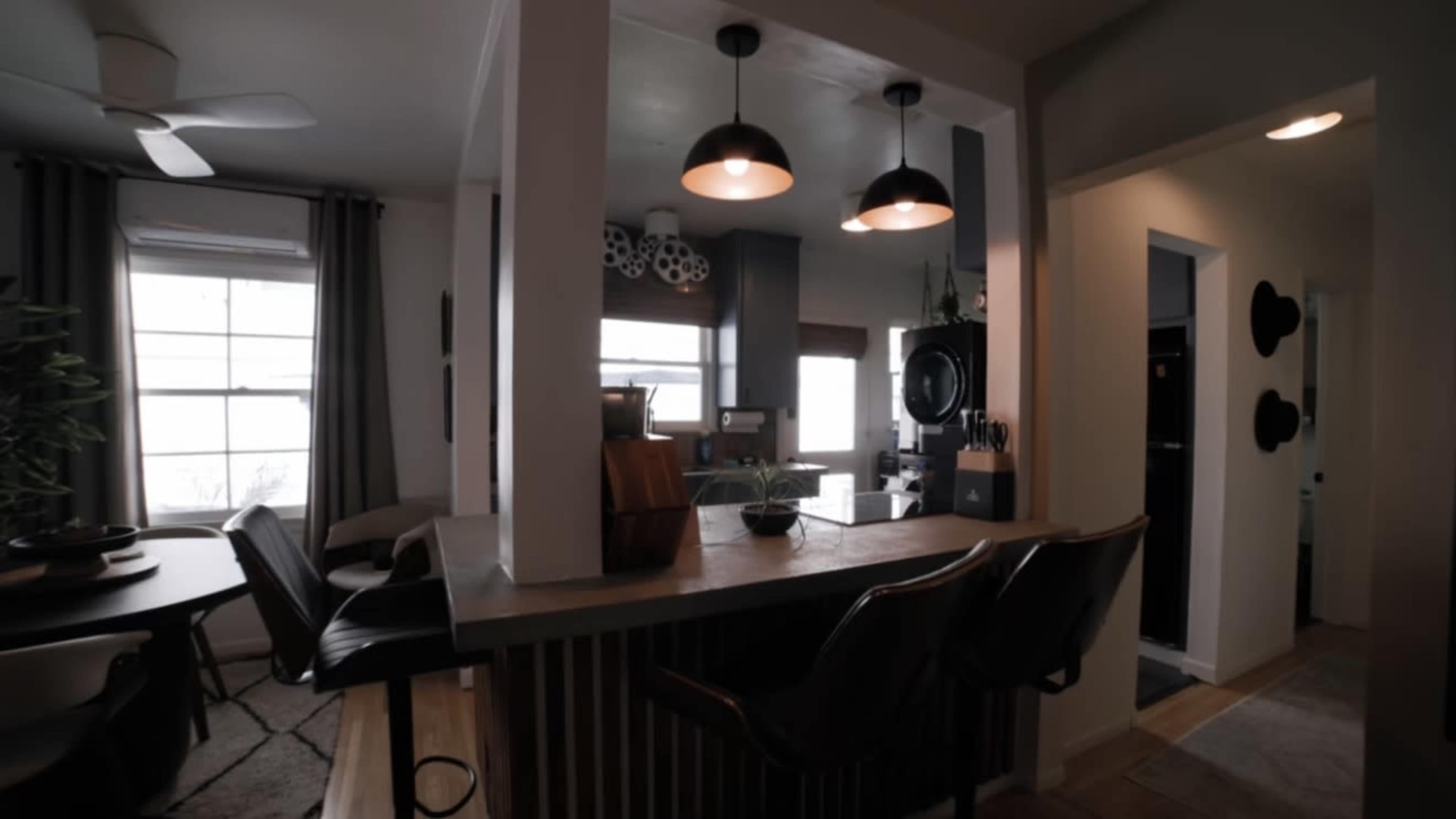 The image shows a modern kitchen and dining area with a bar-style counter and three pendant lights illuminating the space.