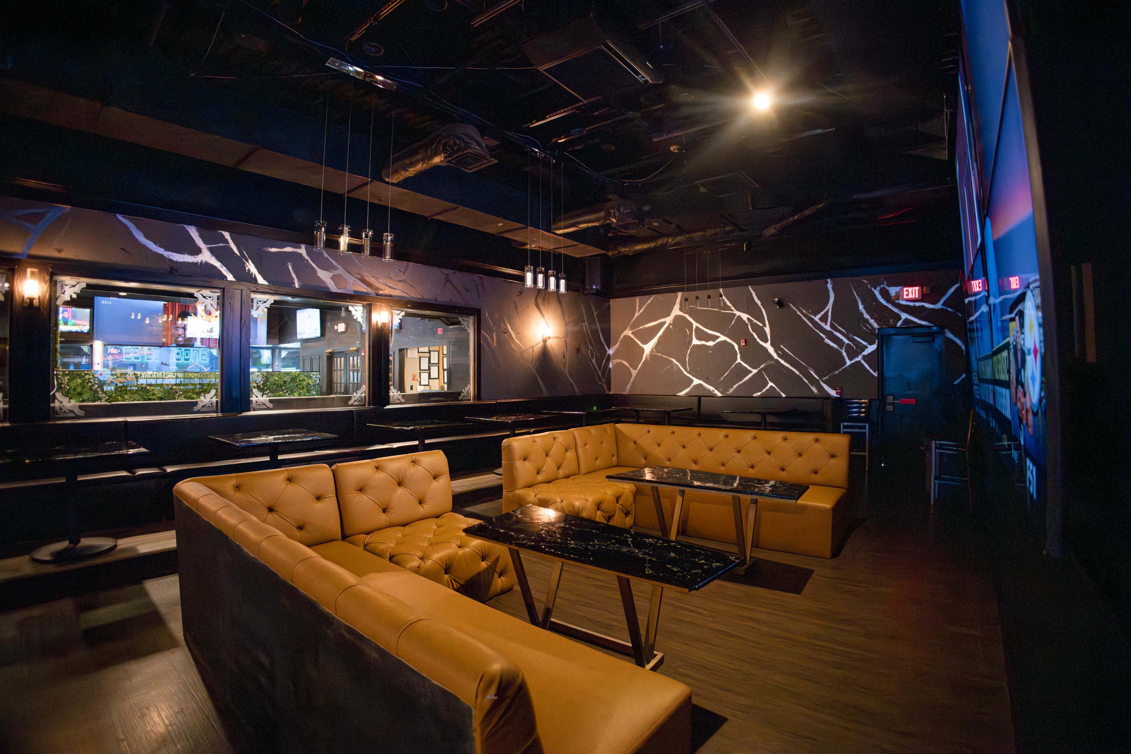 The image shows a dimly lit lounge with a large, tufted leather seating area and a dark, abstract wall design.