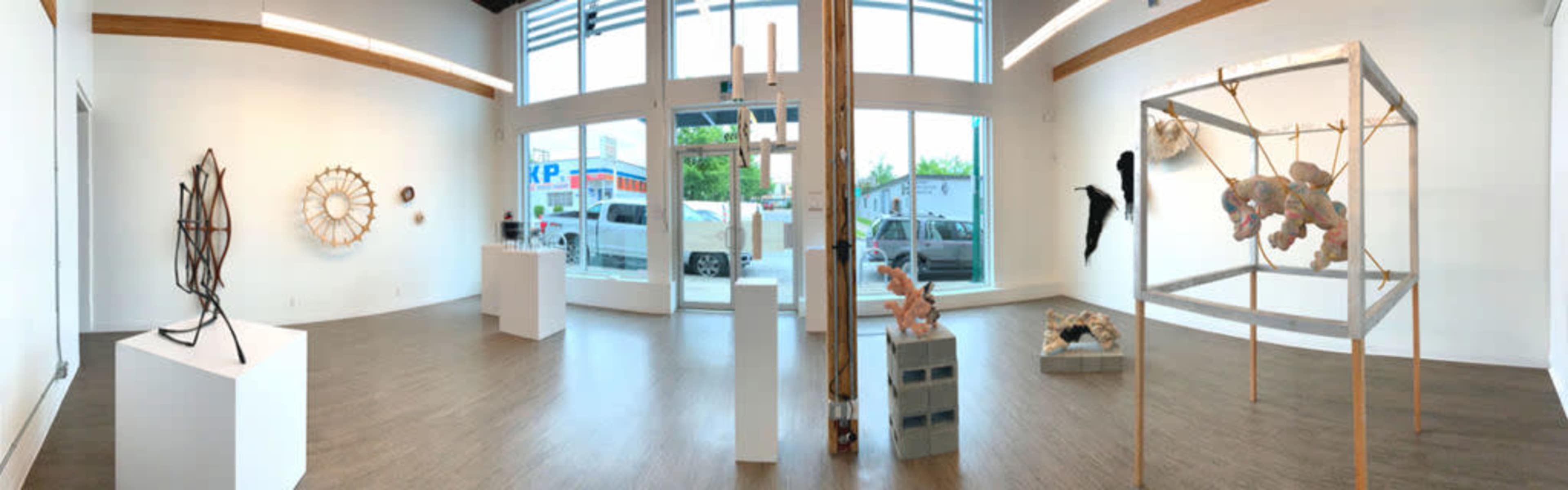 An art gallery interior featuring various sculptures and artworks displayed on white pedestals against a backdrop of large windows.