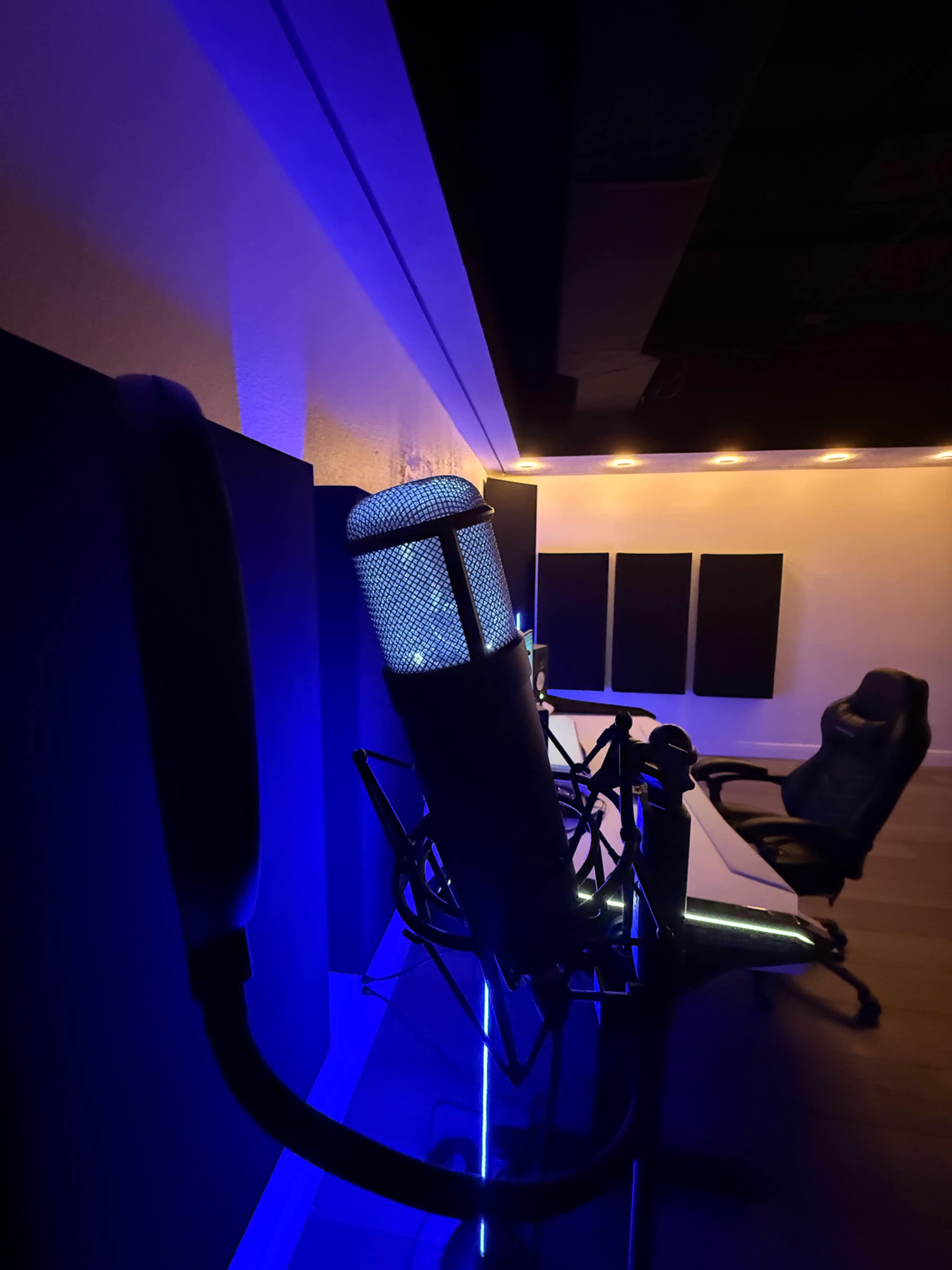 A microphone is positioned in a dimly lit recording studio, with blue and warm lighting illuminating the space.