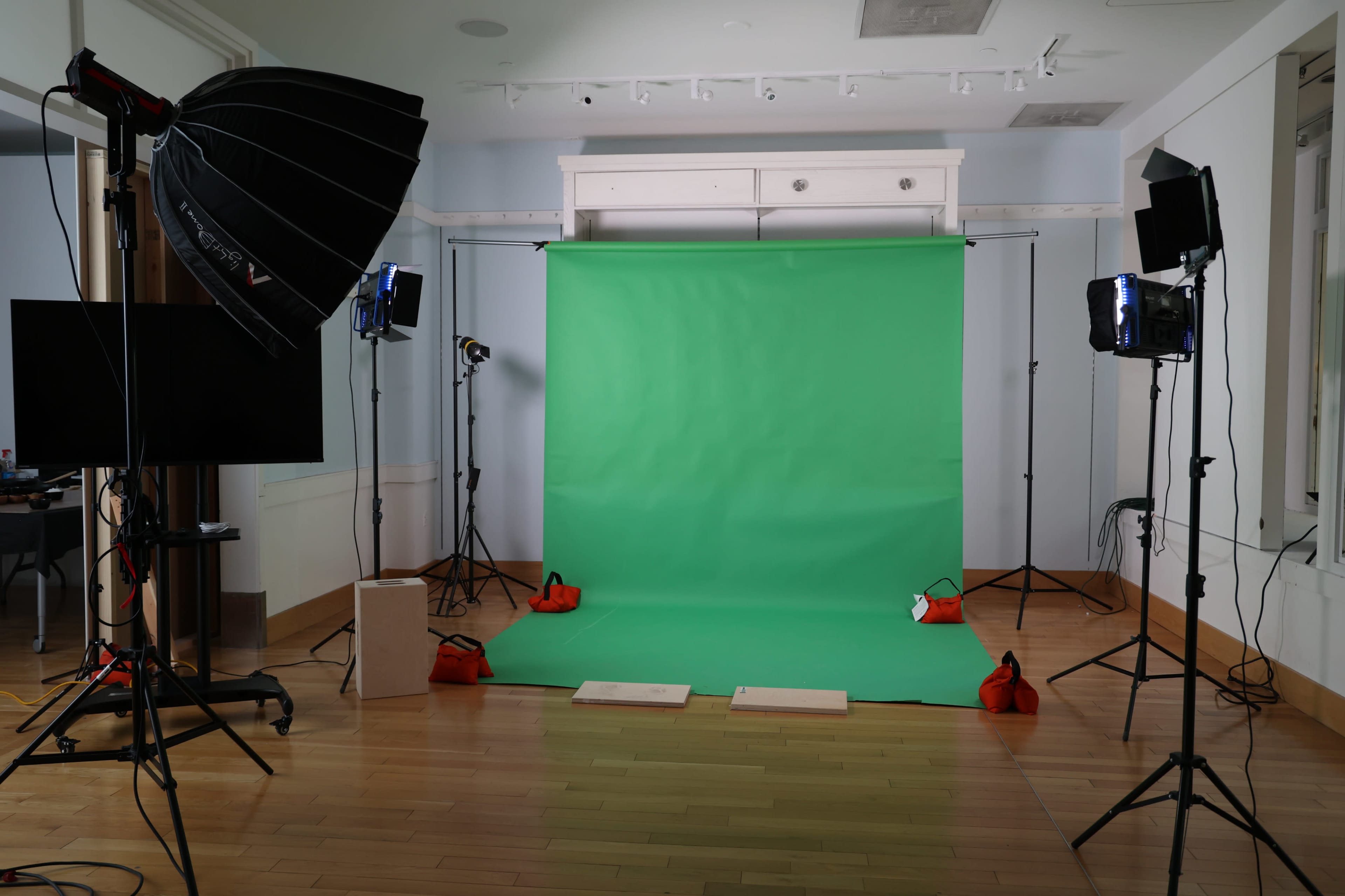 The image shows a photo studio setup with a green backdrop, studio lights, and various equipment arranged around the area.