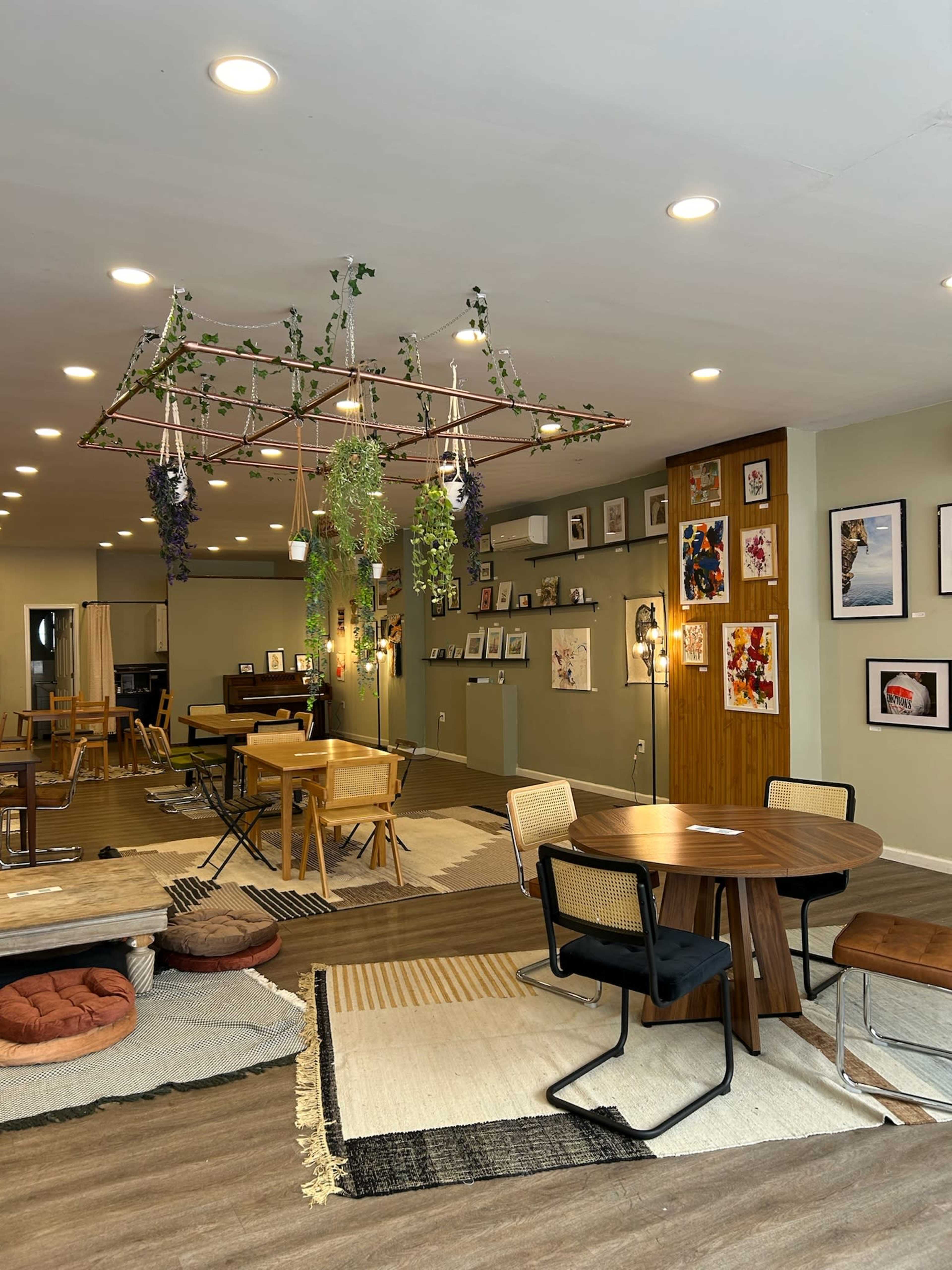 A cozy café with wooden tables, plants hanging from the ceiling, and a wall adorned with framed artwork.