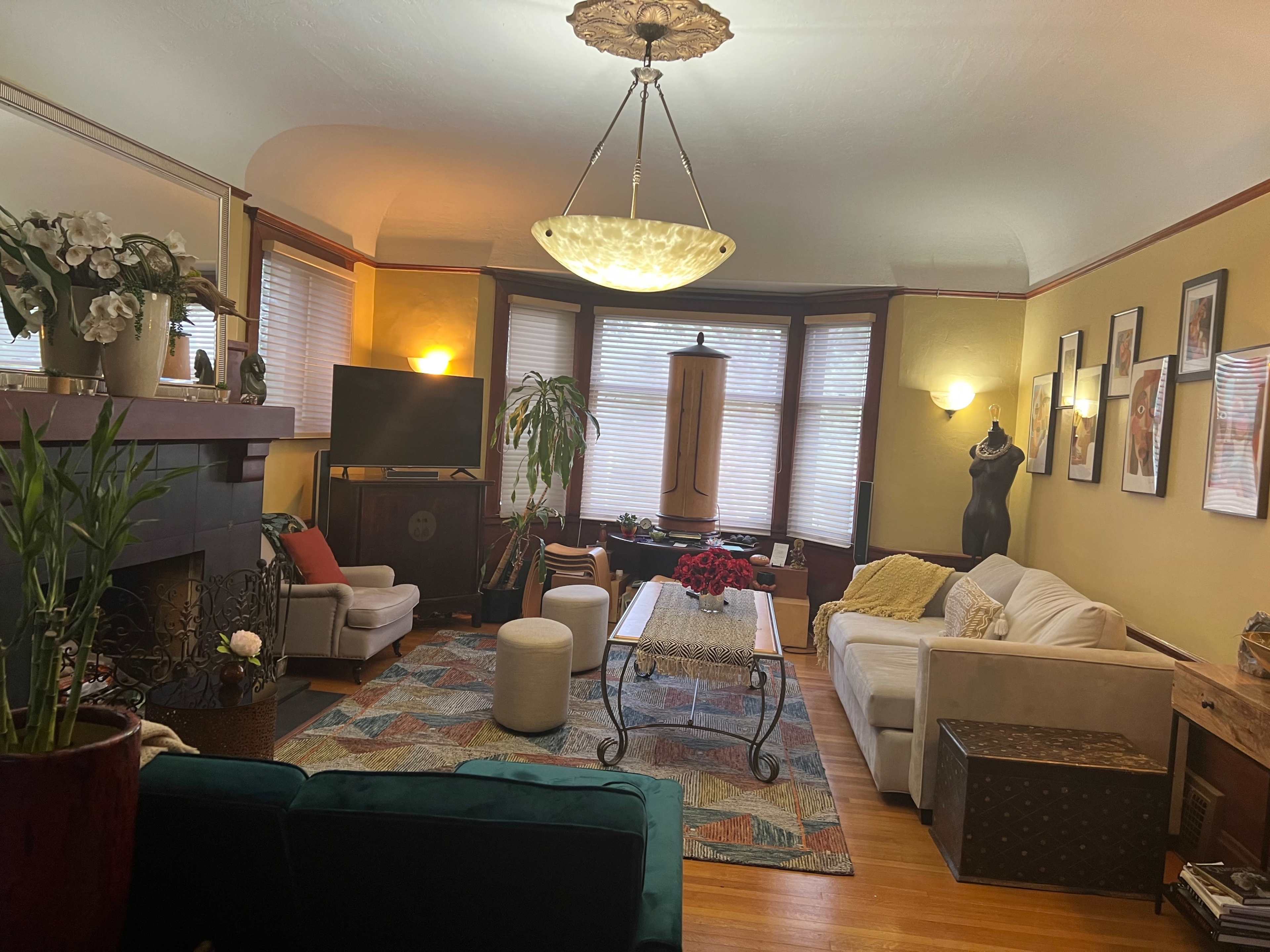 The living room features a mix of seating arrangements, a fireplace, a television, and decorative plants.