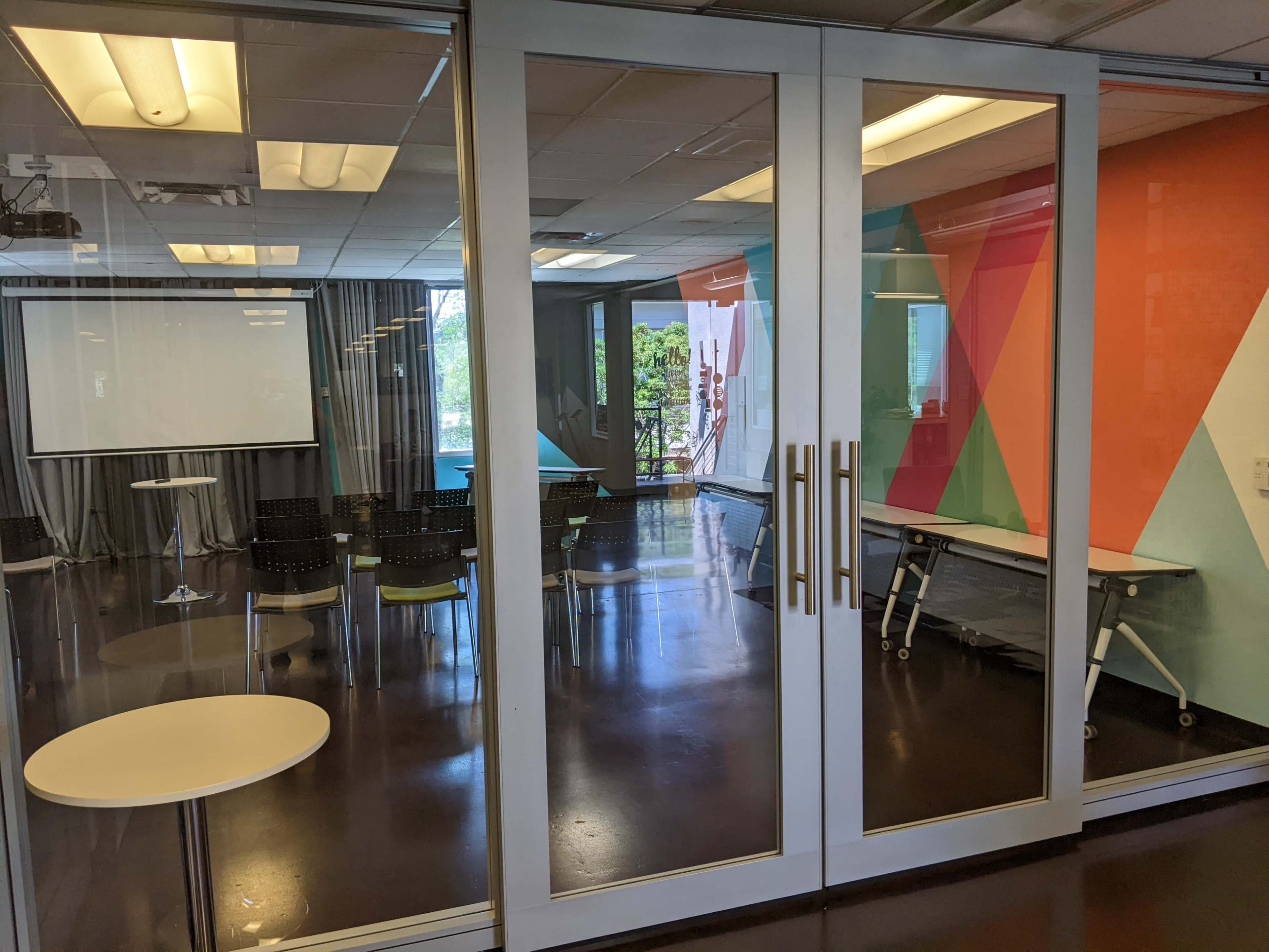 A glass-walled conference room with a modern design, featuring a table, chairs, and a colorful accent wall.