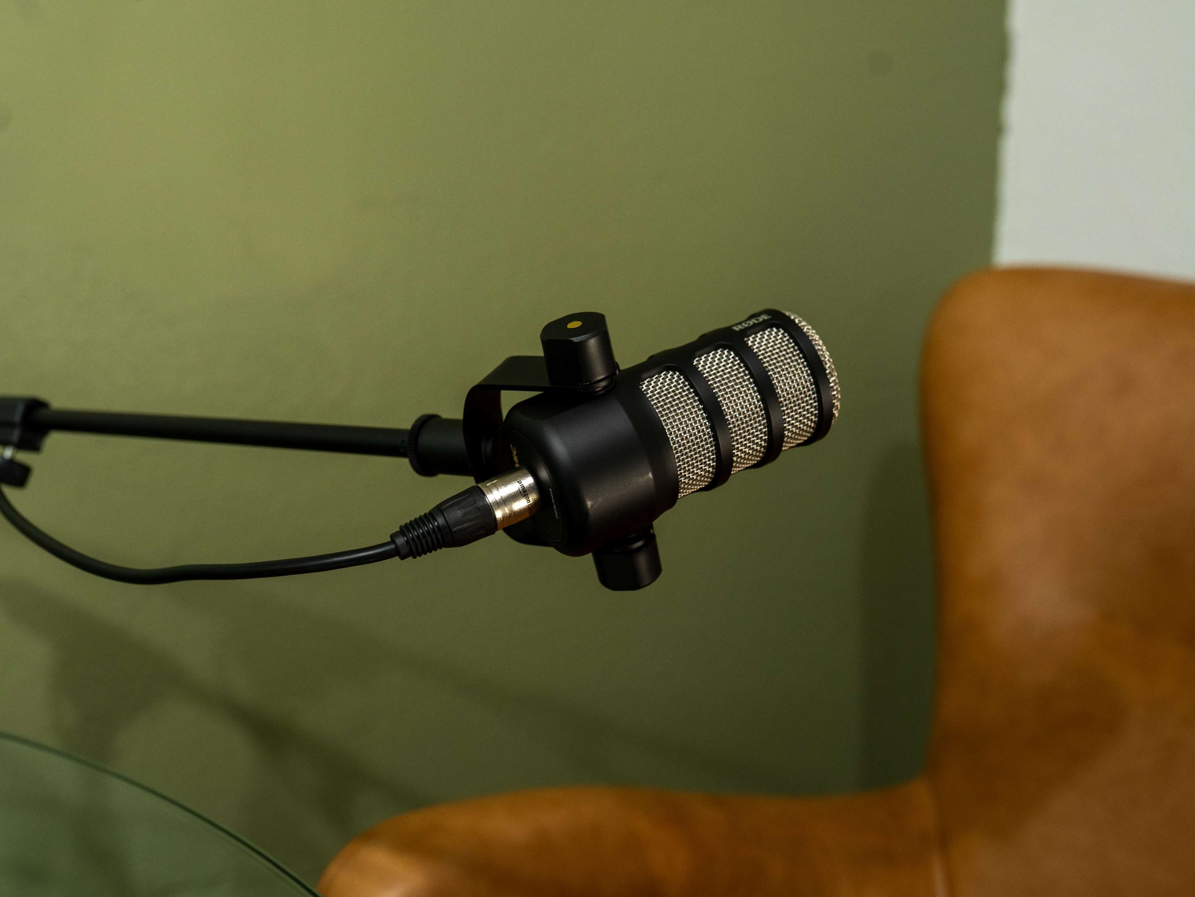 A close-up image of a microphone mounted on an adjustable arm next to a brown chair and a glass table.