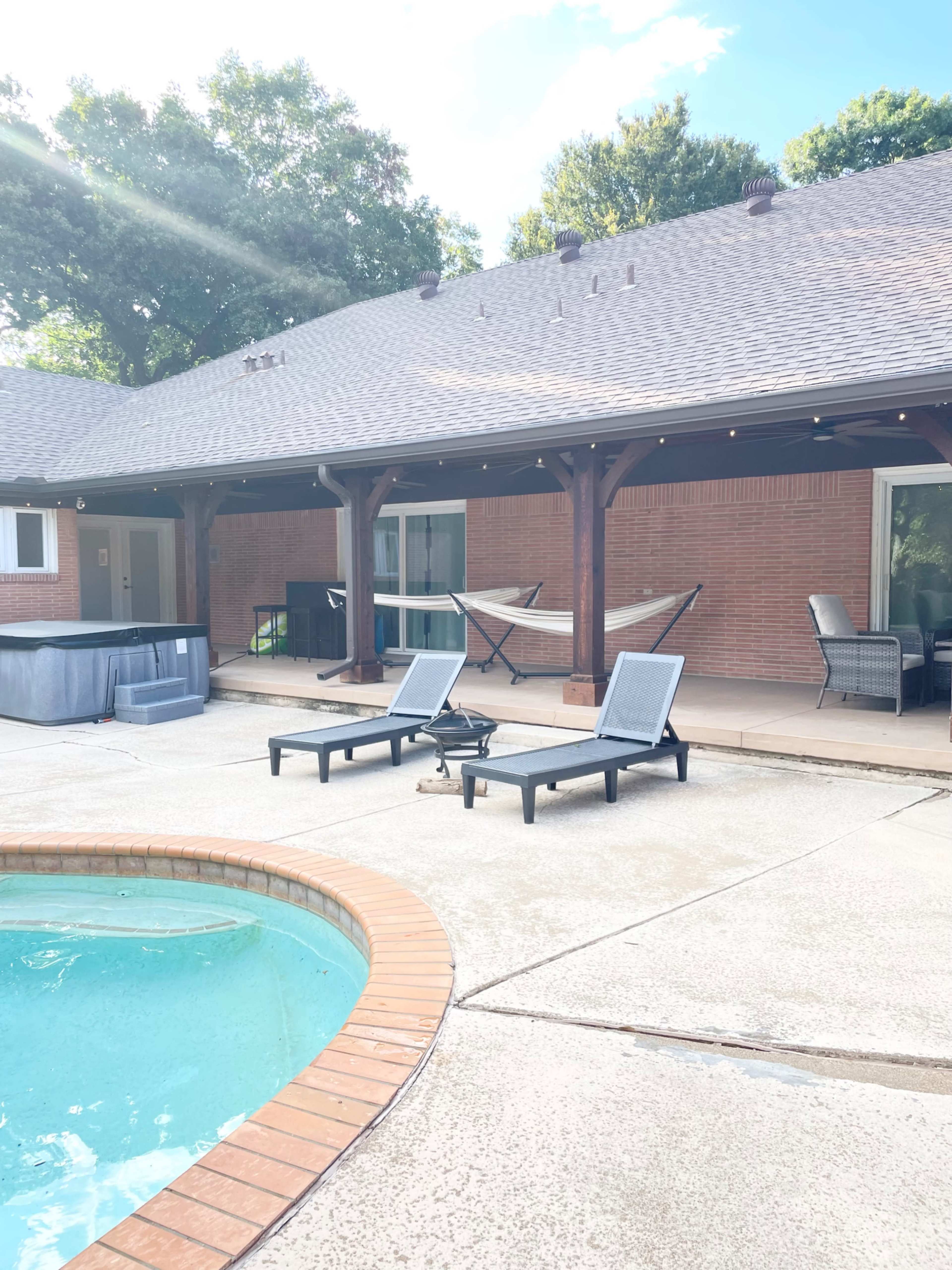 The image shows a backyard patio with a pool, lounge chairs, a hammock, and a hot tub, all set against a house with a sloped roof.