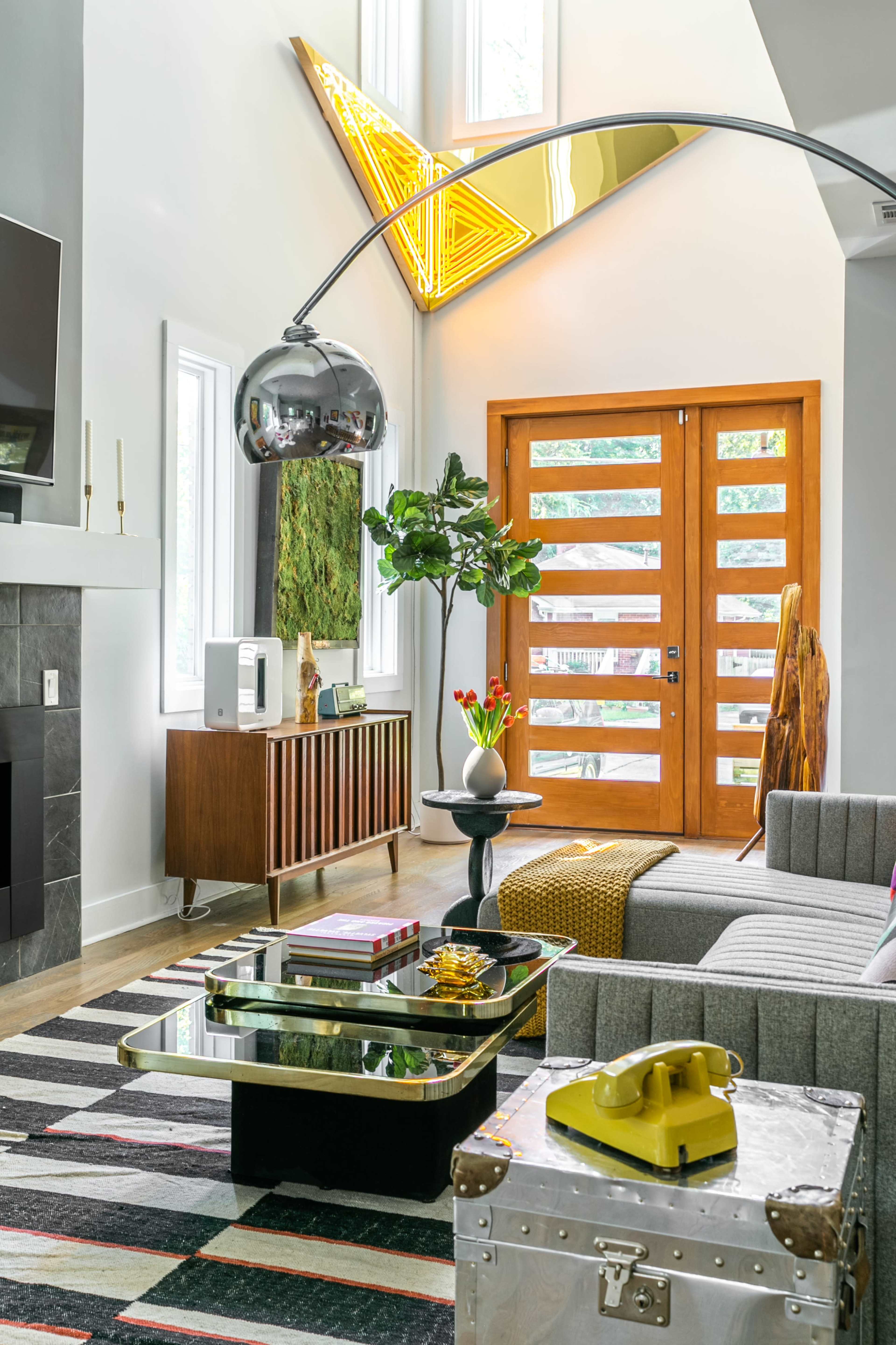 A modern living room features a striped rug, a gray sectional sofa, a coffee table, and a wooden door with geometric cutouts.