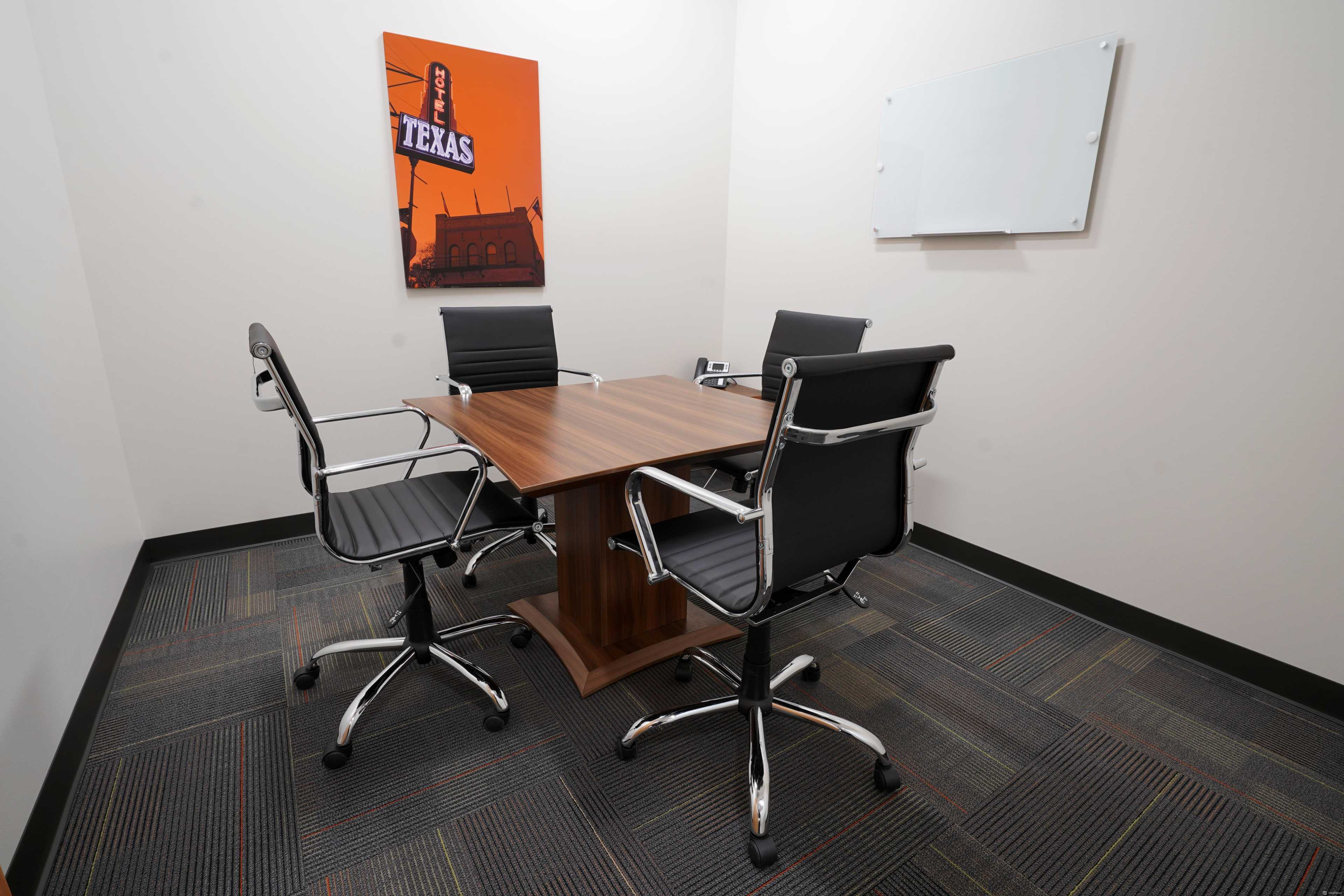 A small conference room features a wooden table surrounded by three black office chairs and a Texas-themed artwork on the wall.