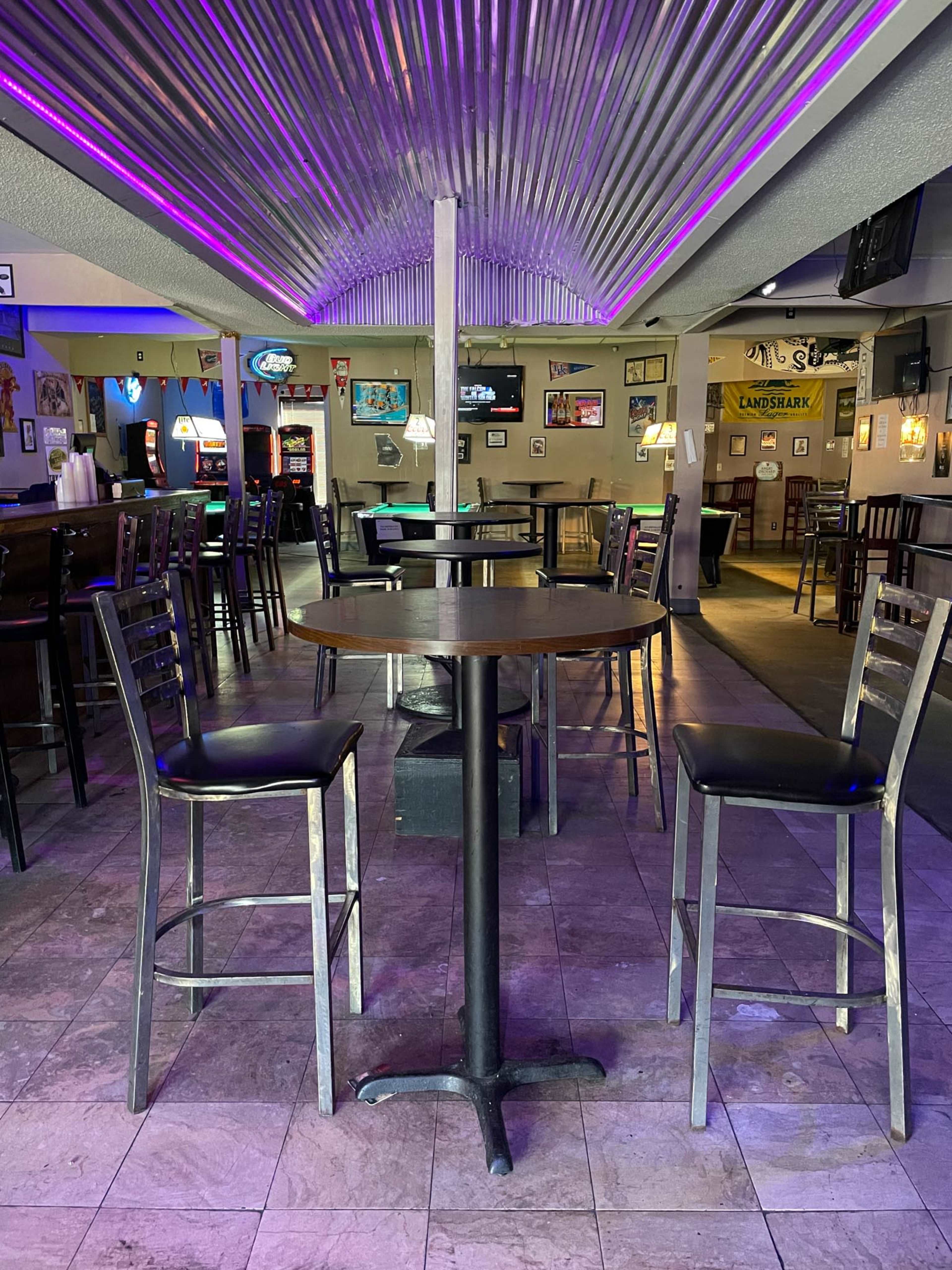An empty bar area with a circular table and four high stools under a metallic ceiling.