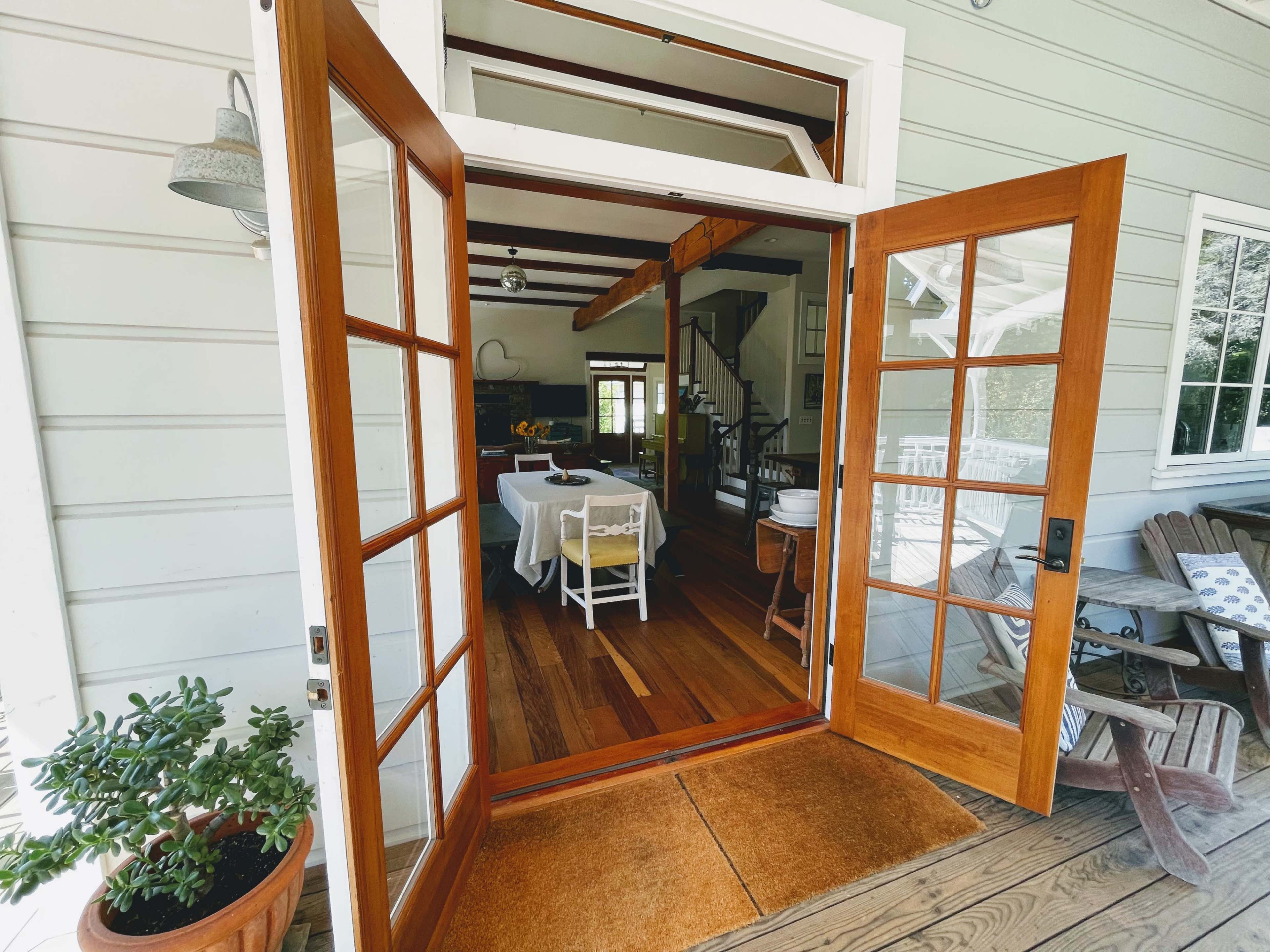 An open double door leads into a dining area with a table set for meals, framed by wooden flooring and a staircase in the background.