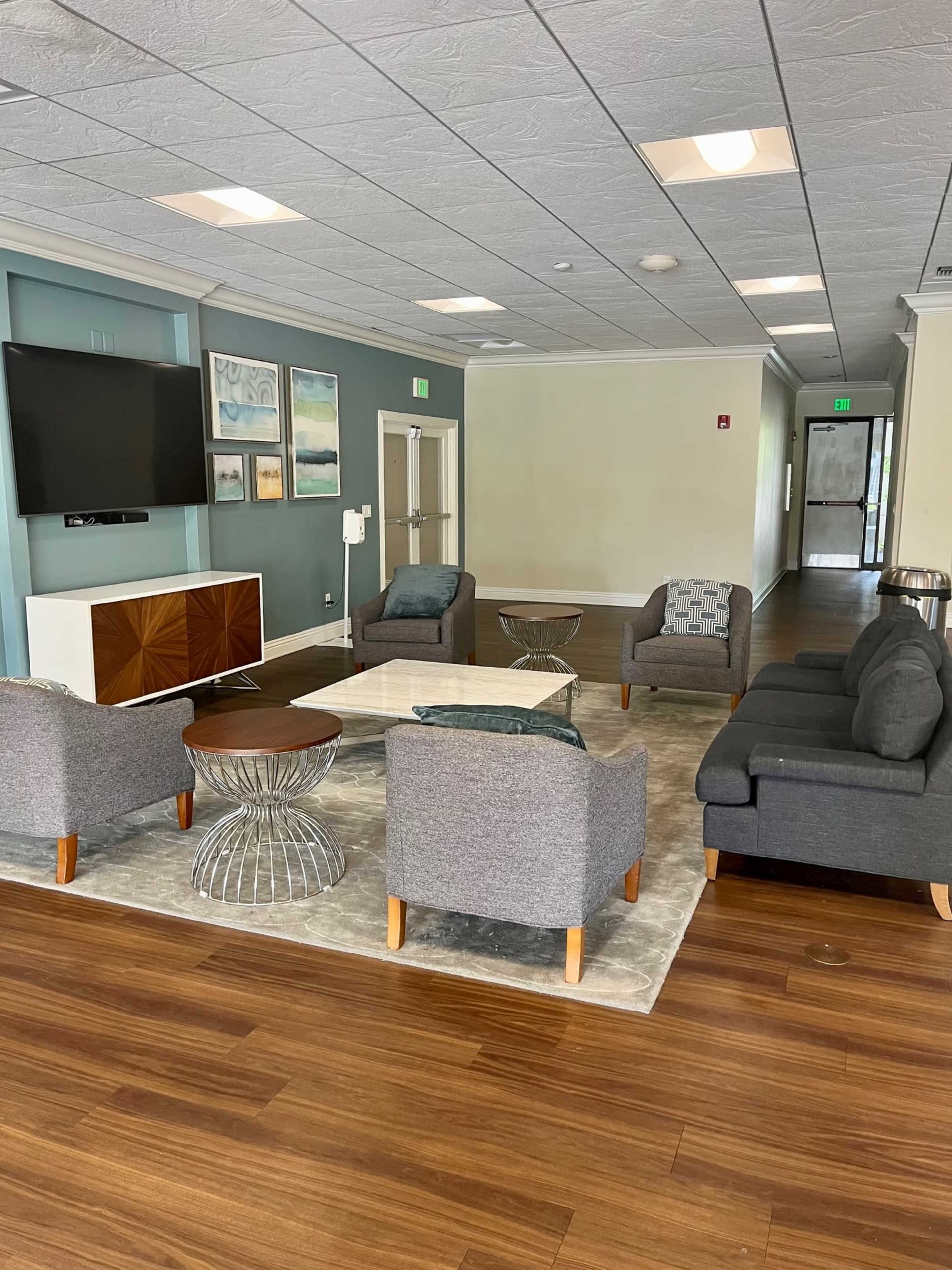 A modern lounge area with gray upholstered sofas, a coffee table, and a large wall-mounted television.