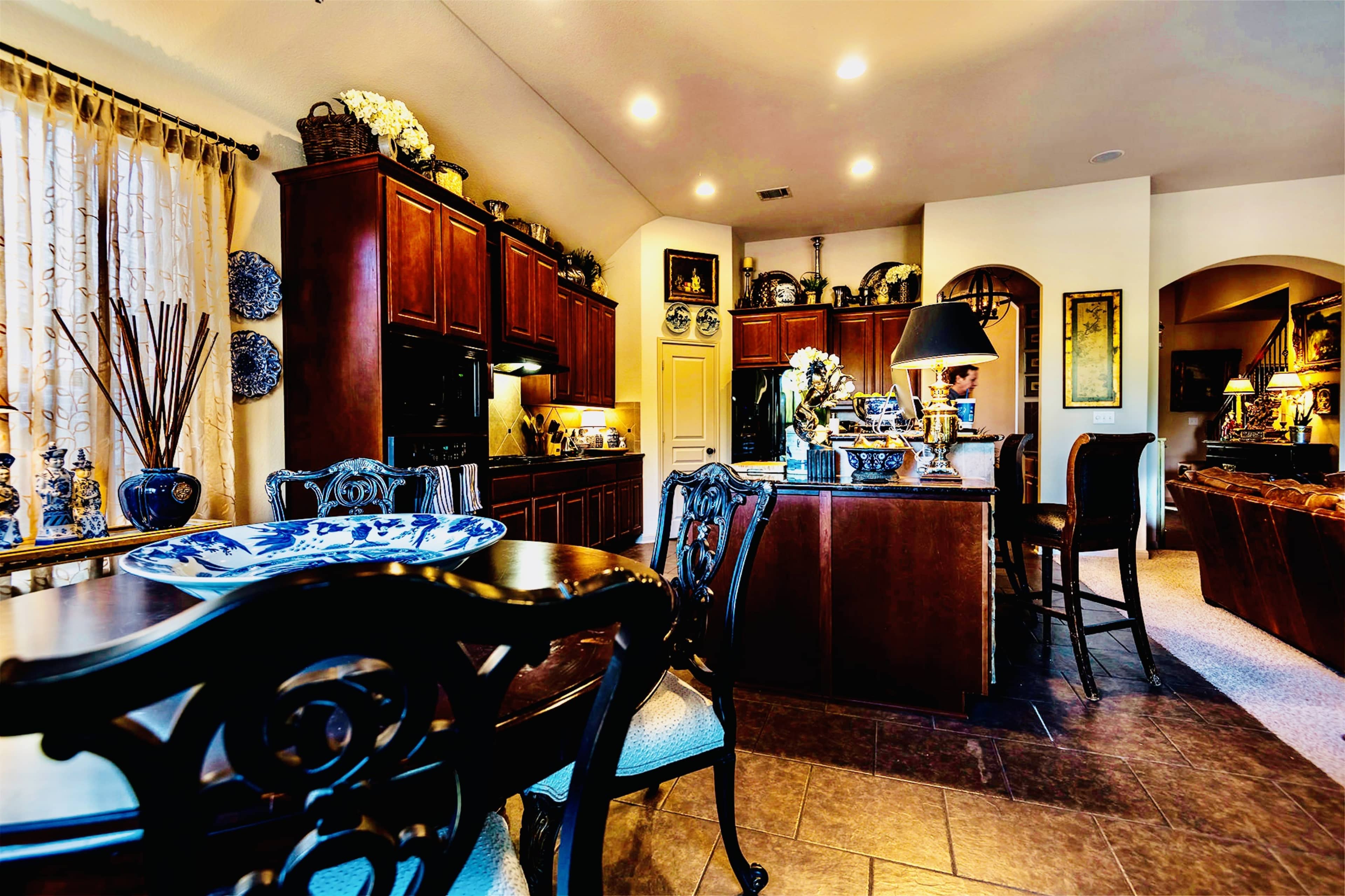 A kitchen with dark wooden cabinets, a dining table set for four, and decorative items displayed on the countertops and shelves.