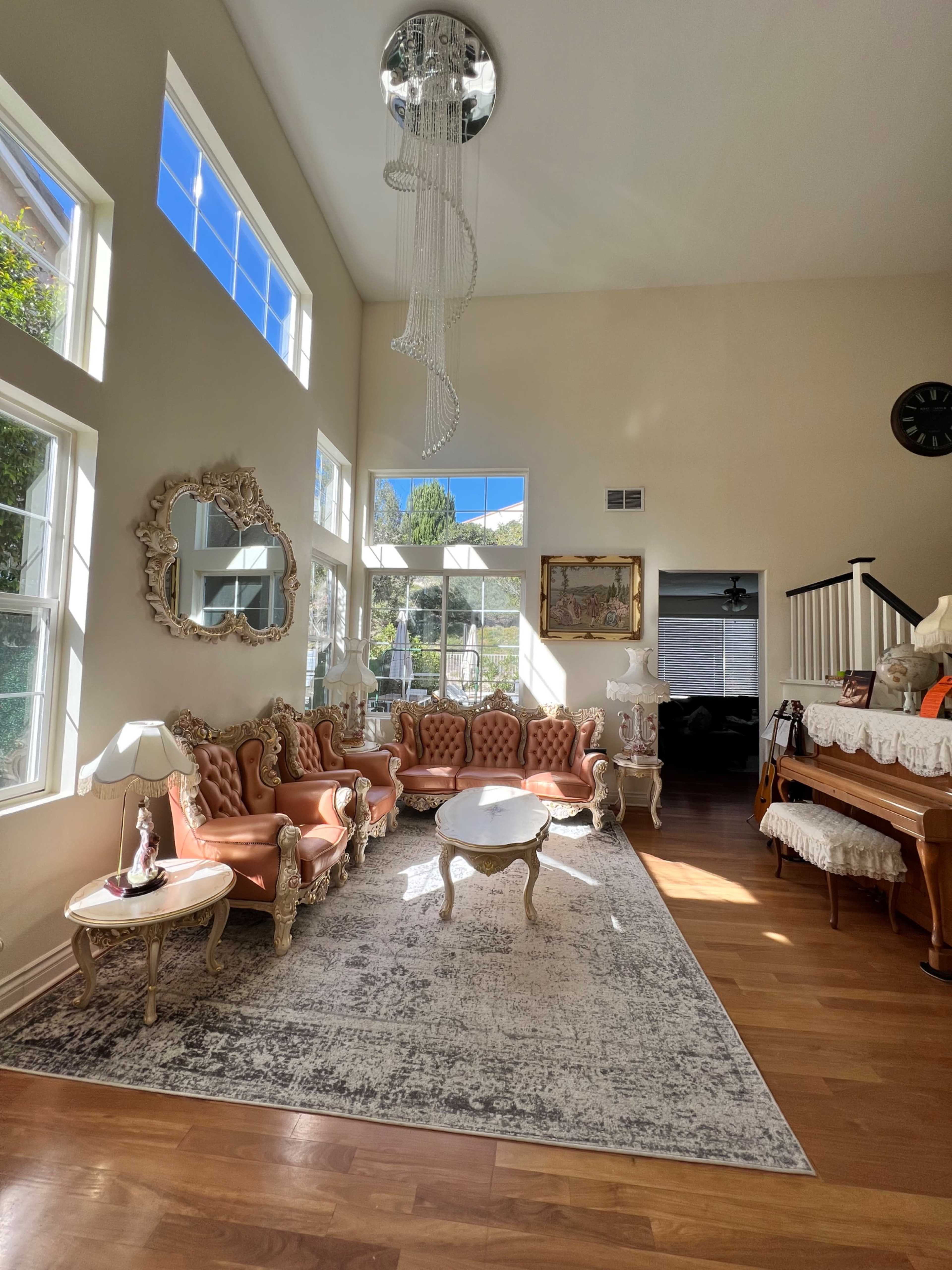 A spacious living room with large windows, featuring a set of pink tufted sofas, a round coffee table, a piano, and decorative art on the walls.