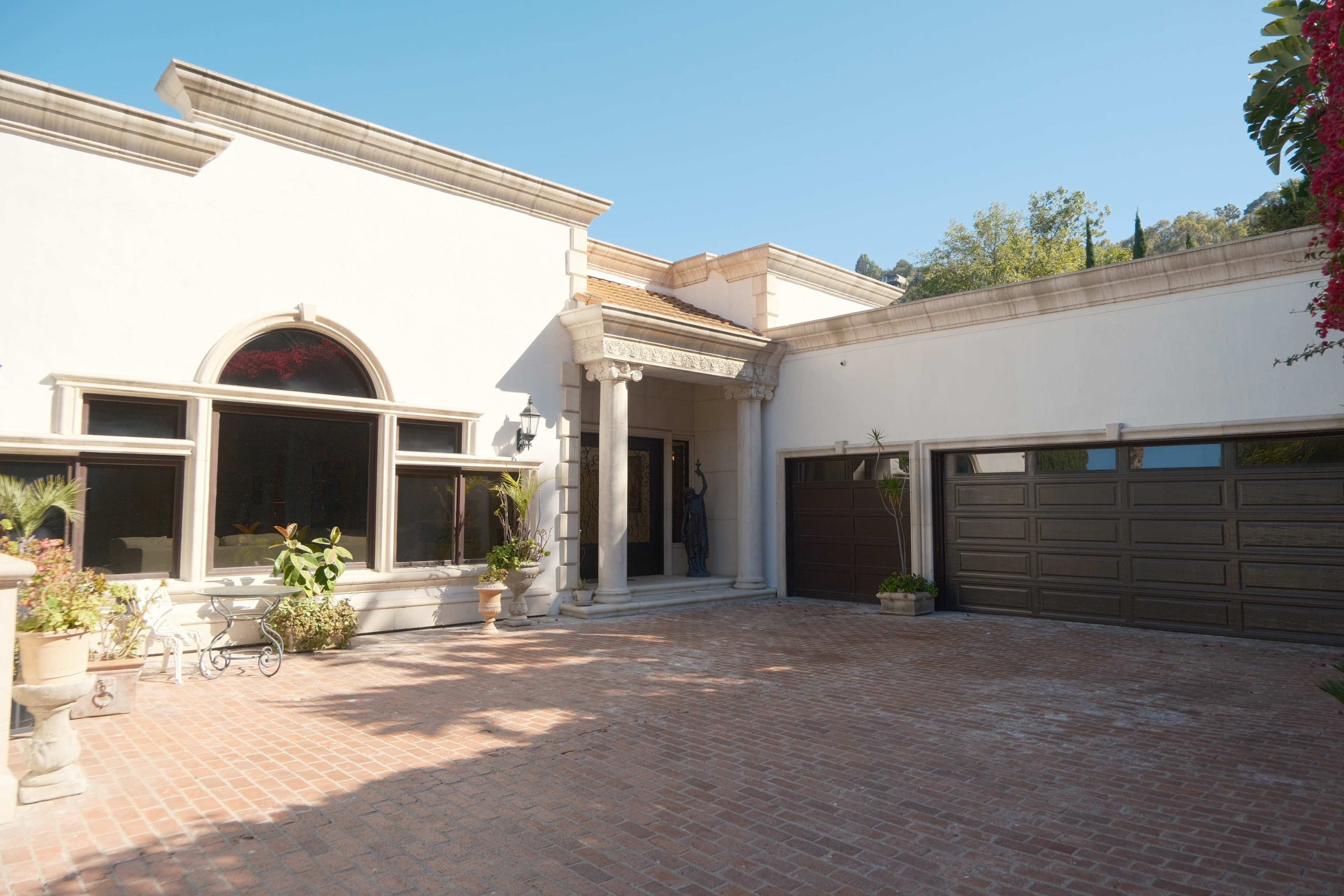 The image shows a large home with a distinctive entrance featuring arched windows and a spacious brick driveway.