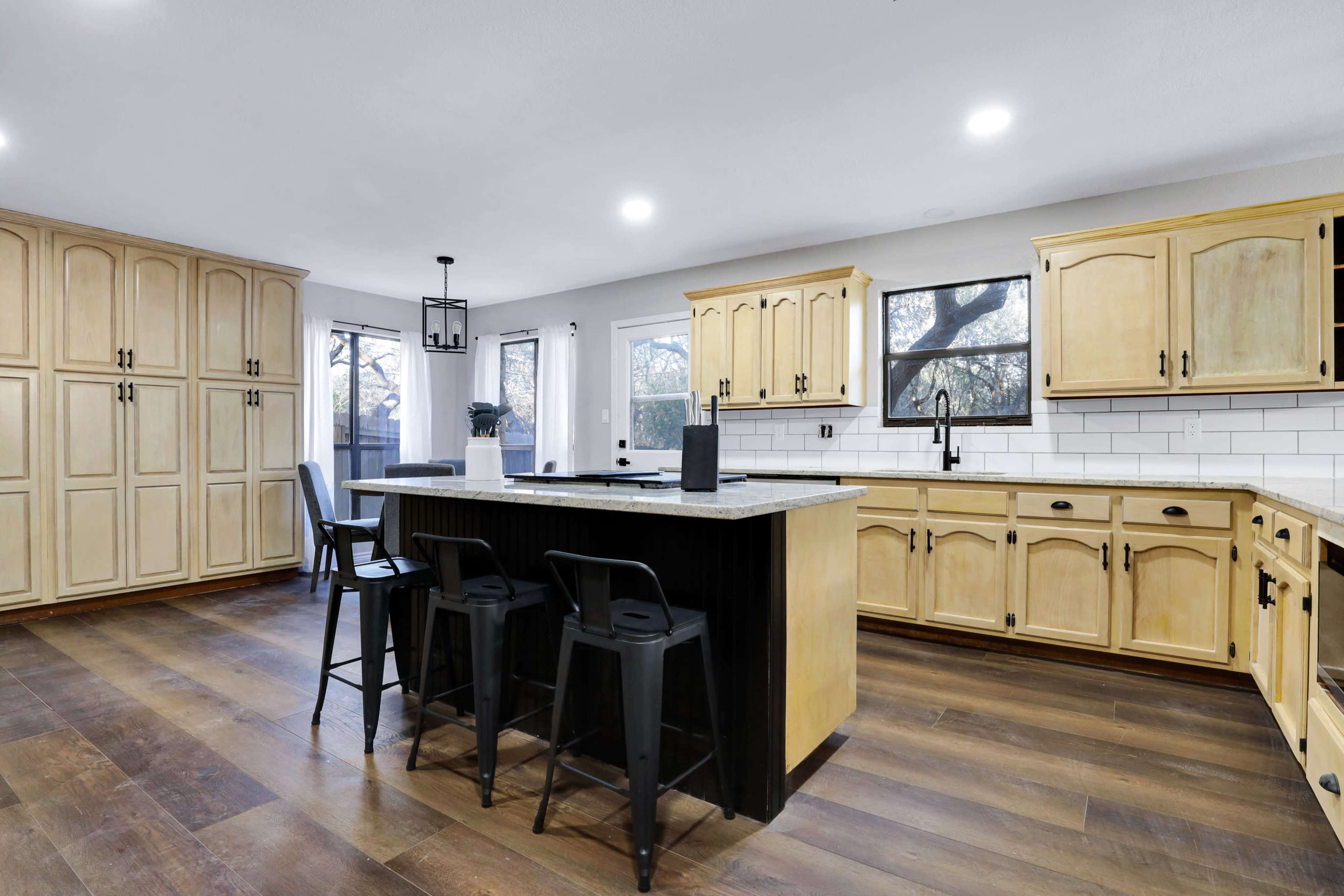 A modern kitchen features wooden cabinetry, a central island with bar stools, and stainless steel appliances.