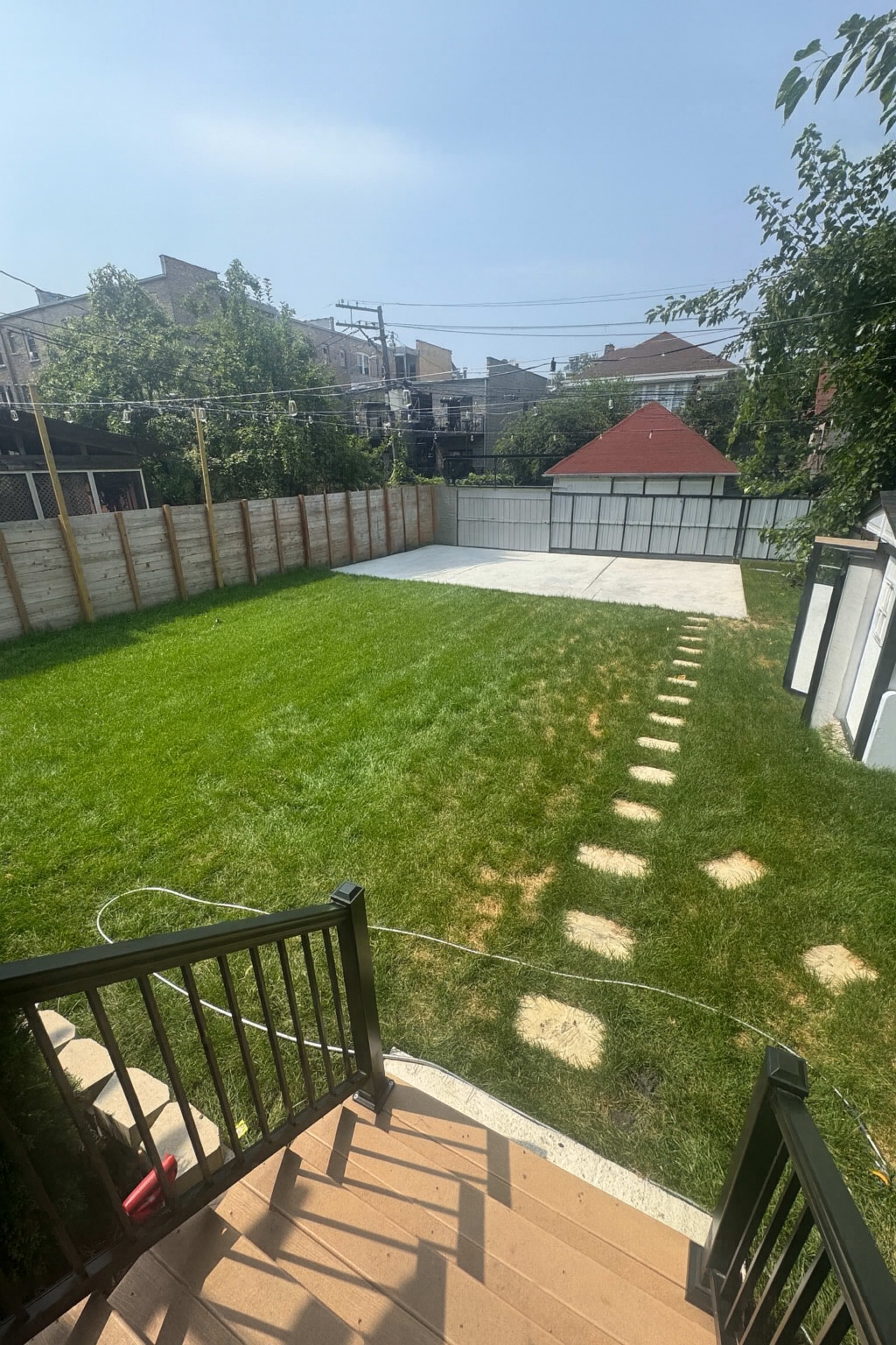 The image shows a spacious backyard with a green lawn, a concrete area, and a wooden fence surrounding the property.