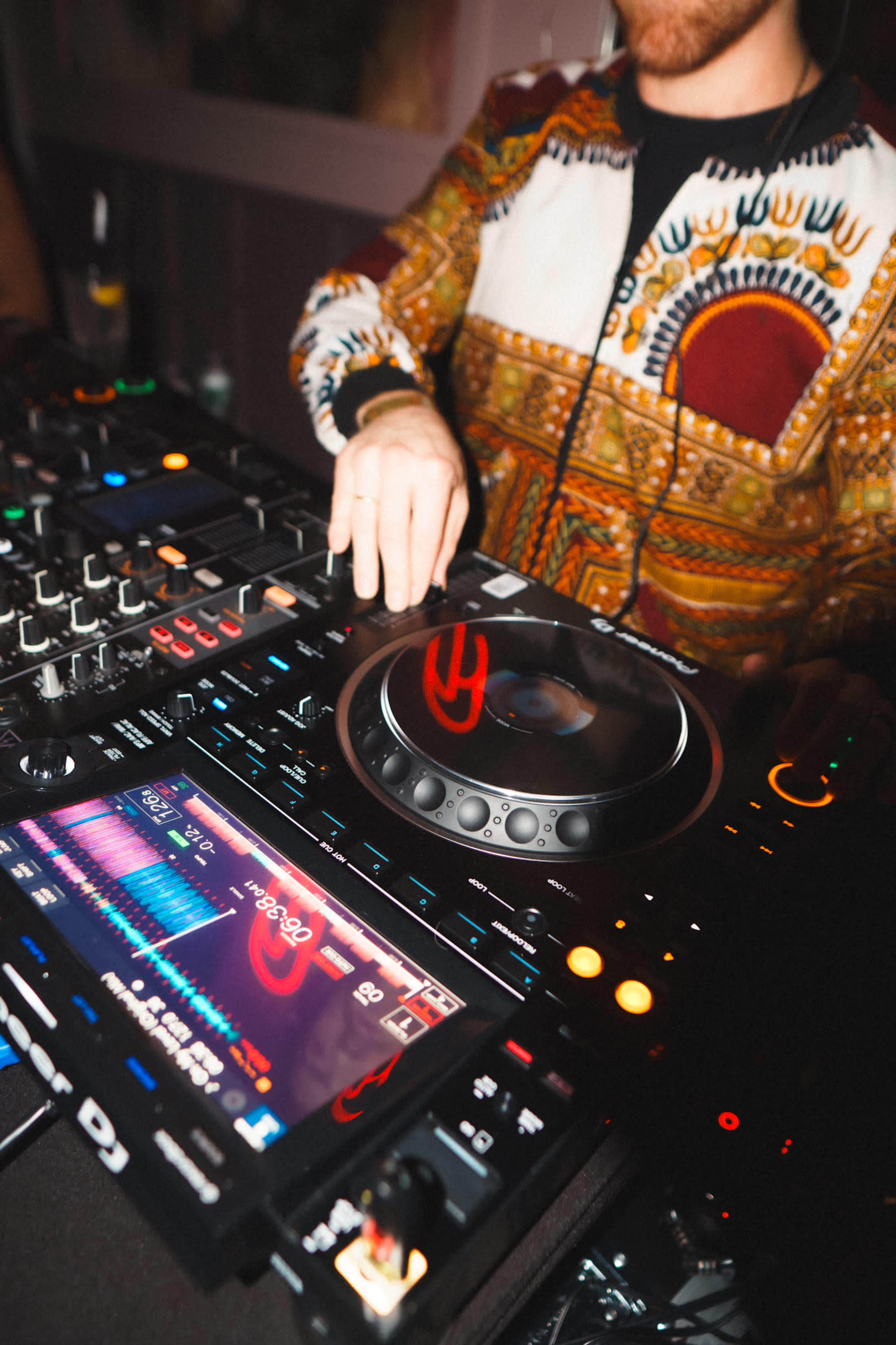 A DJ is mixing music at a turntable, wearing a colorful patterned jacket.