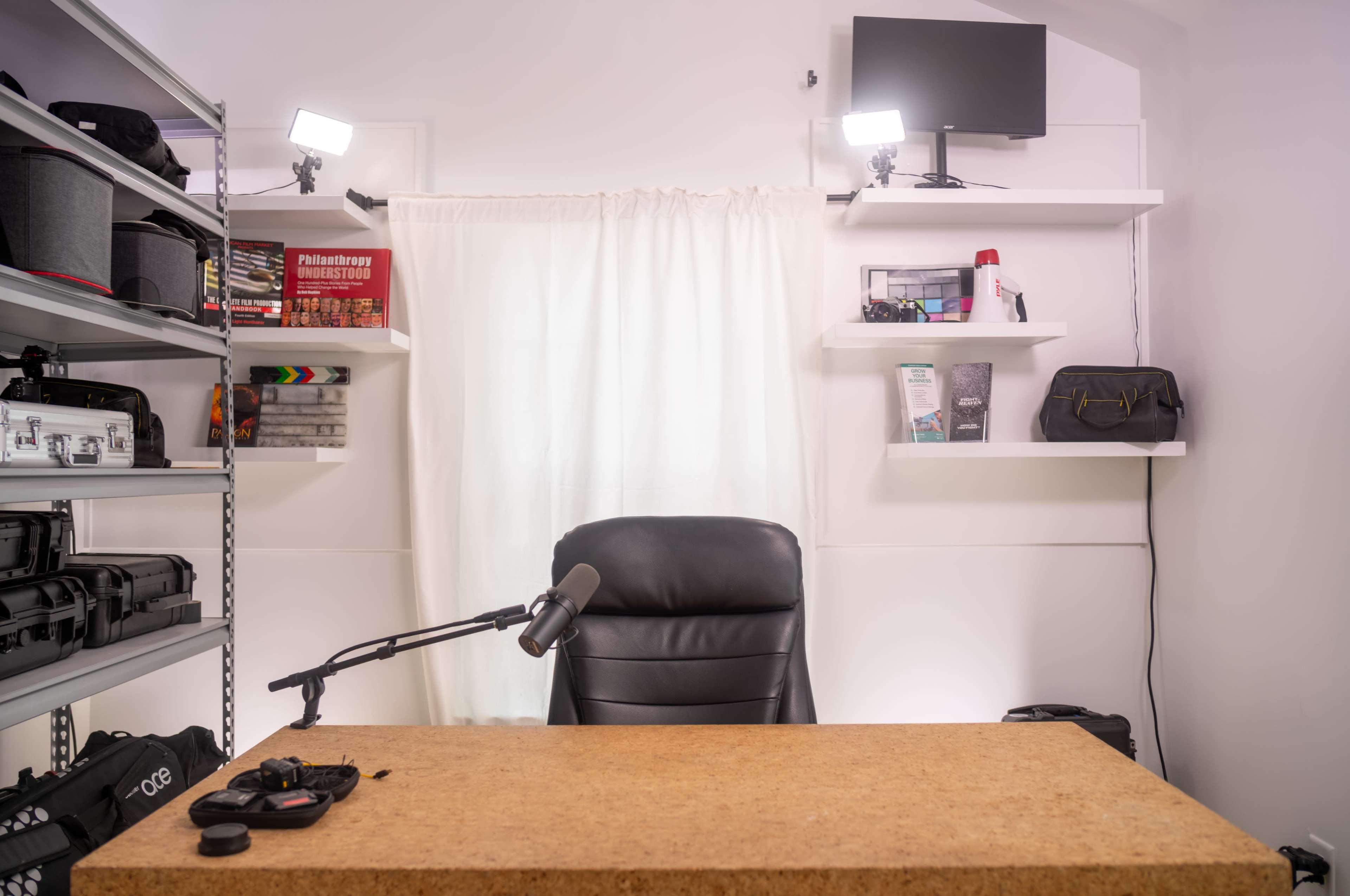 The image shows an empty workspace with a black chair, a microphone on the desk, and shelves featuring various items and equipment.