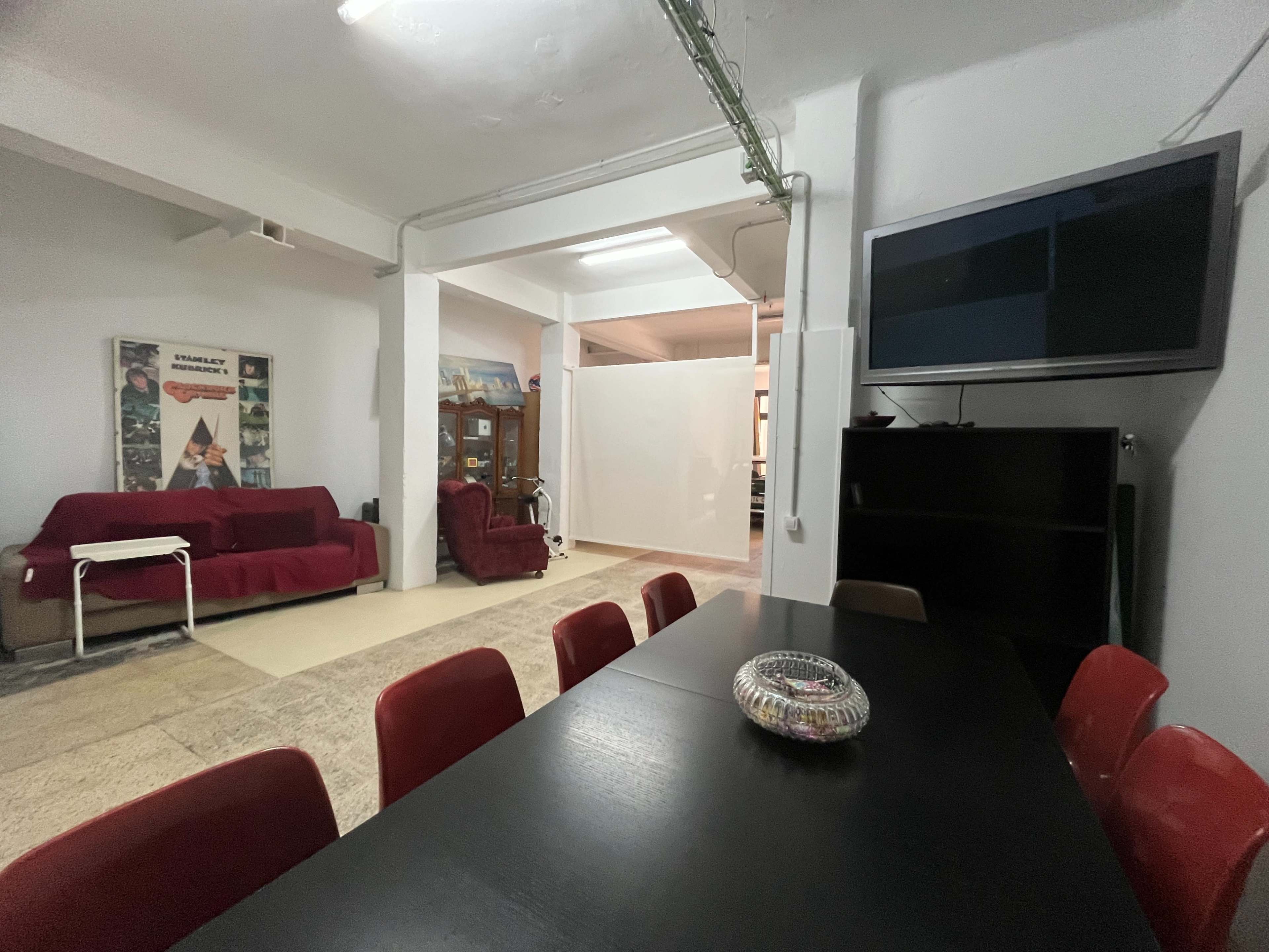 A dining area features a black table surrounded by red chairs, with a couch and television in the background.