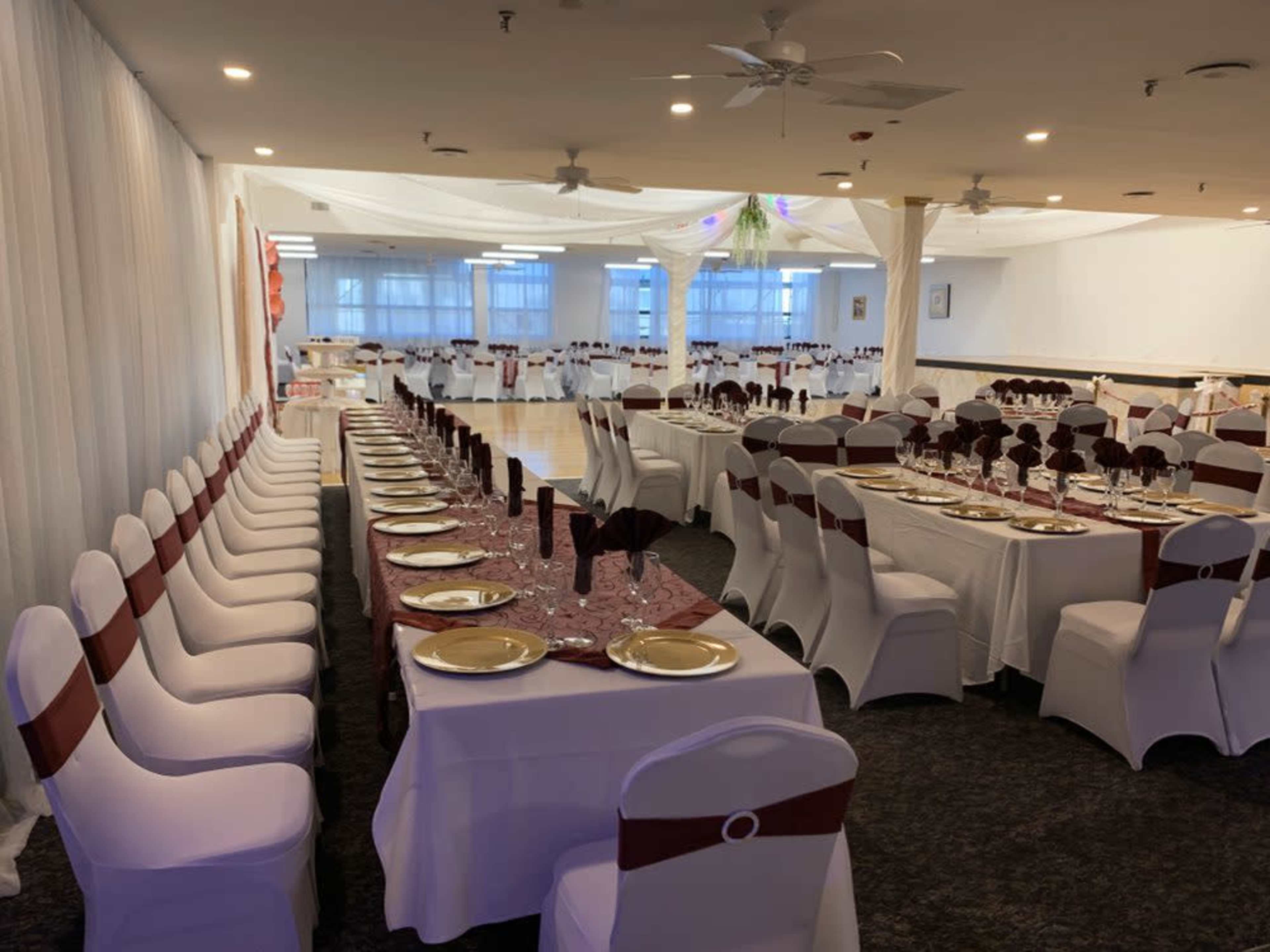 A spacious dining area features multiple tables set with white tablecloths and burgundy accents, arranged for an event.