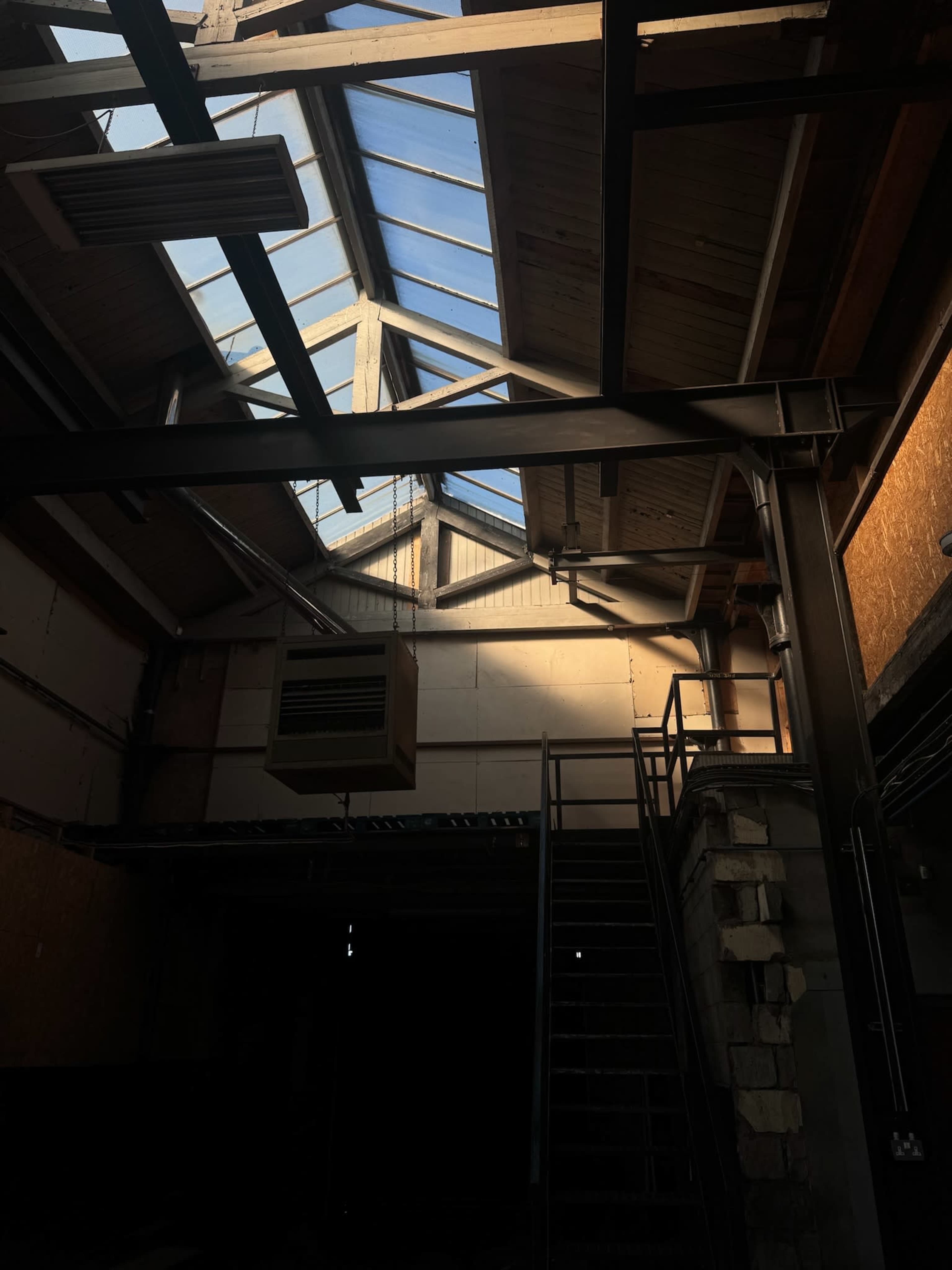An interior of a large industrial space featuring a metal staircase and skylights allowing natural light to filter through.