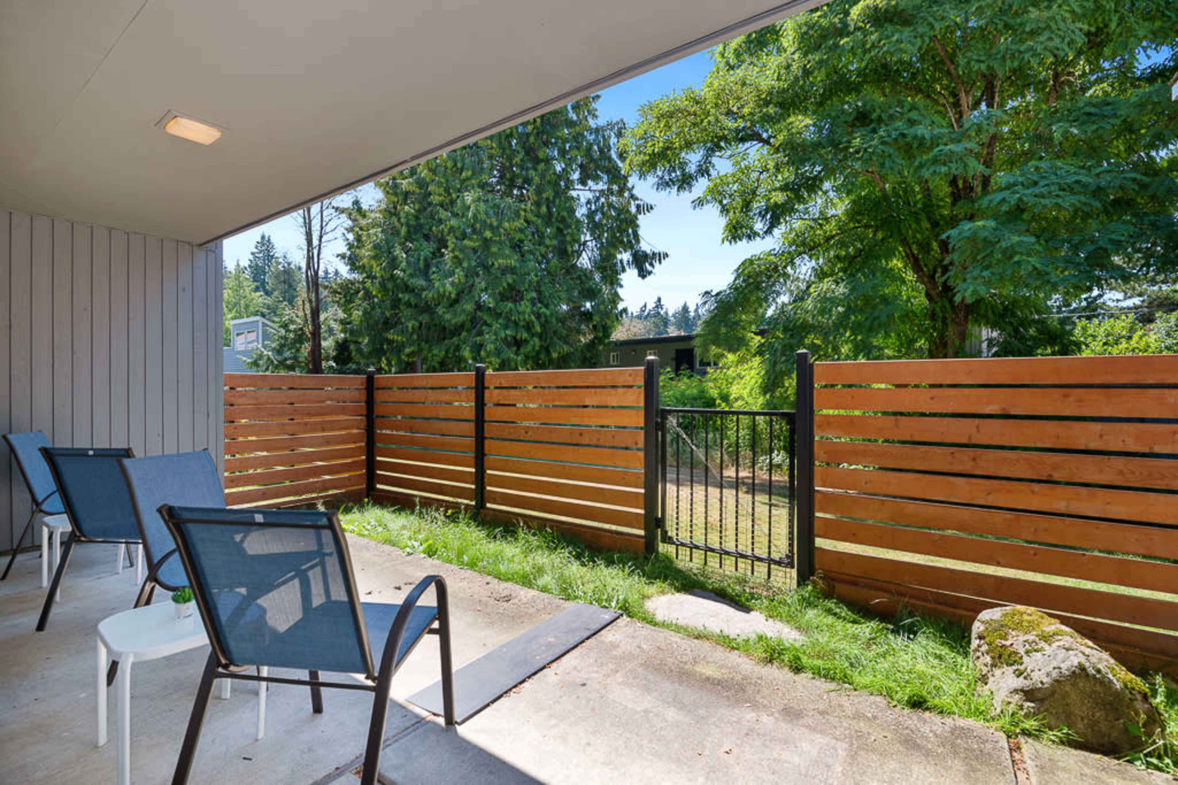 The image shows a patio area with two chairs and a small table overlooking a fenced yard and trees.