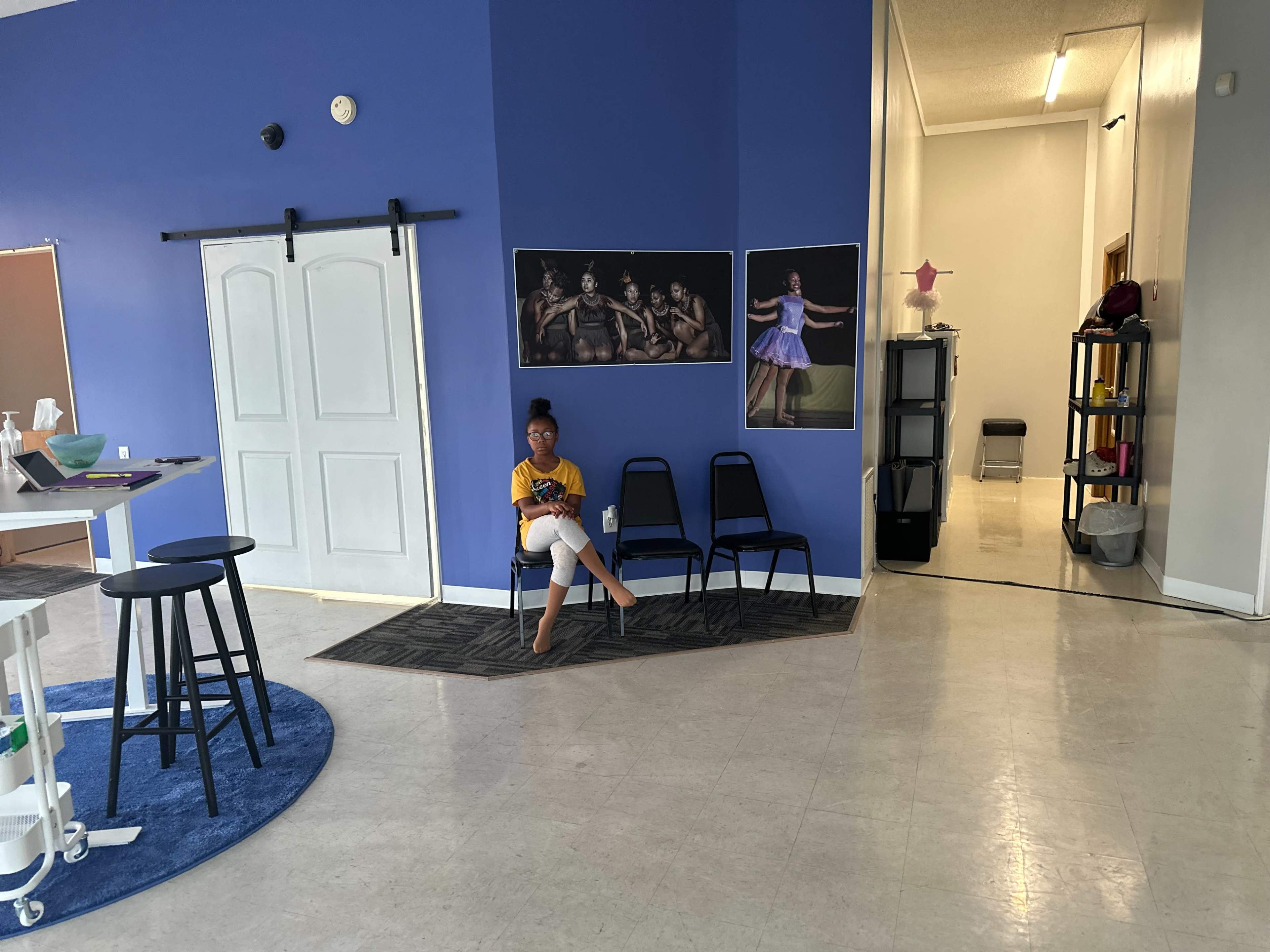 A person sits on a chair in a brightly colored room with blue walls and several framed photographs on display.
