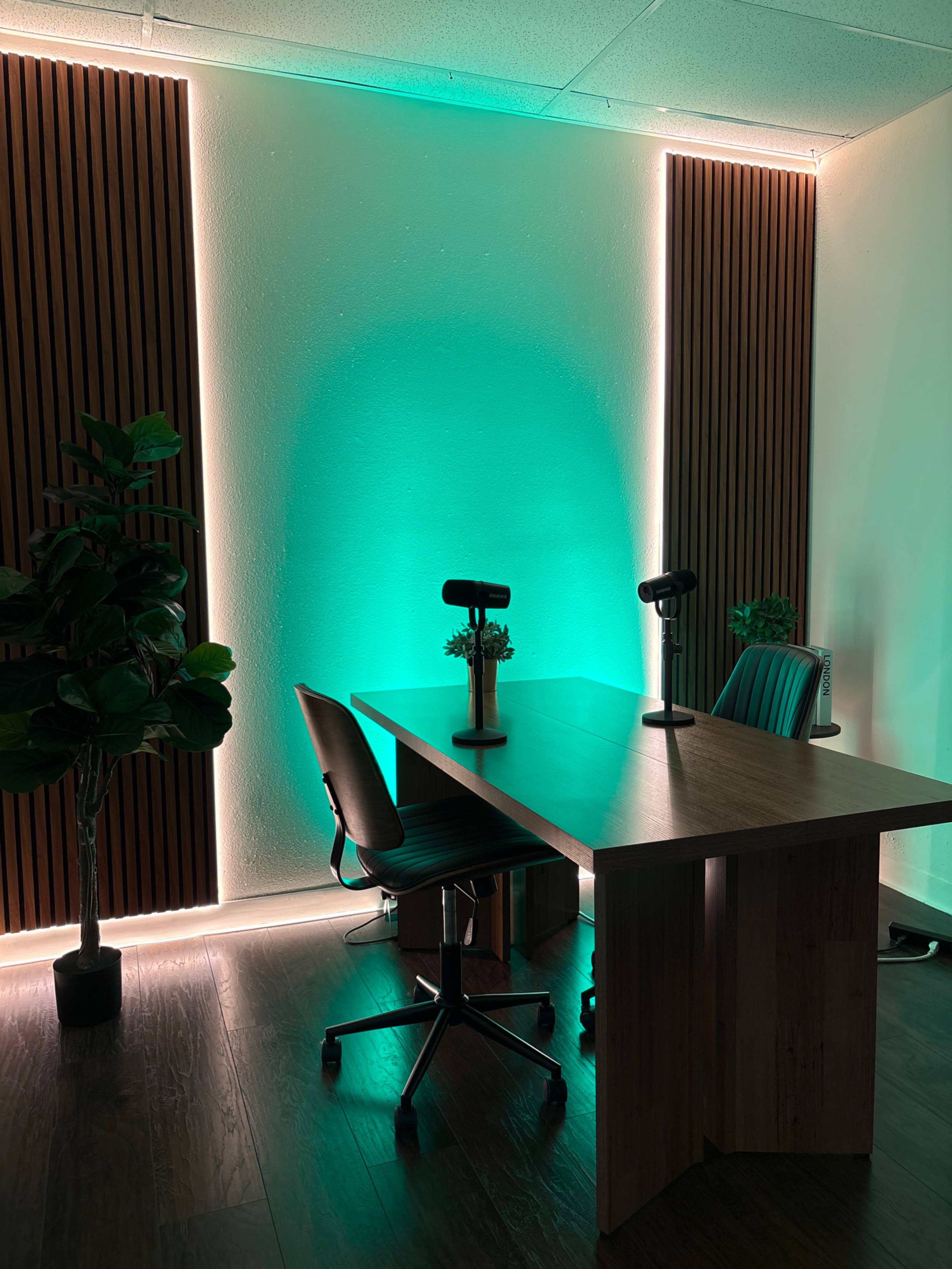 The image shows a modern office space with a wooden table, two chairs, and green ambient lighting along the walls.