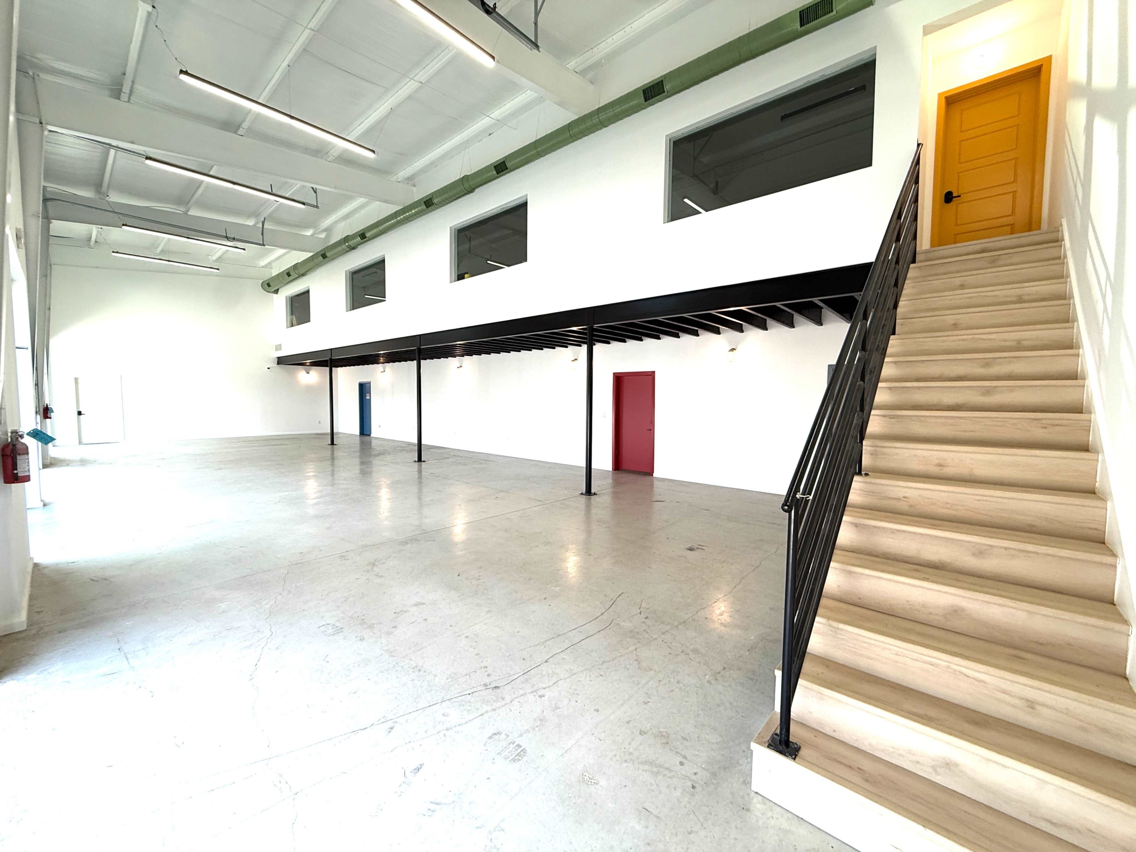 The image shows a spacious interior with a staircase on the right, leading to a second level, and several doorways along the walls.