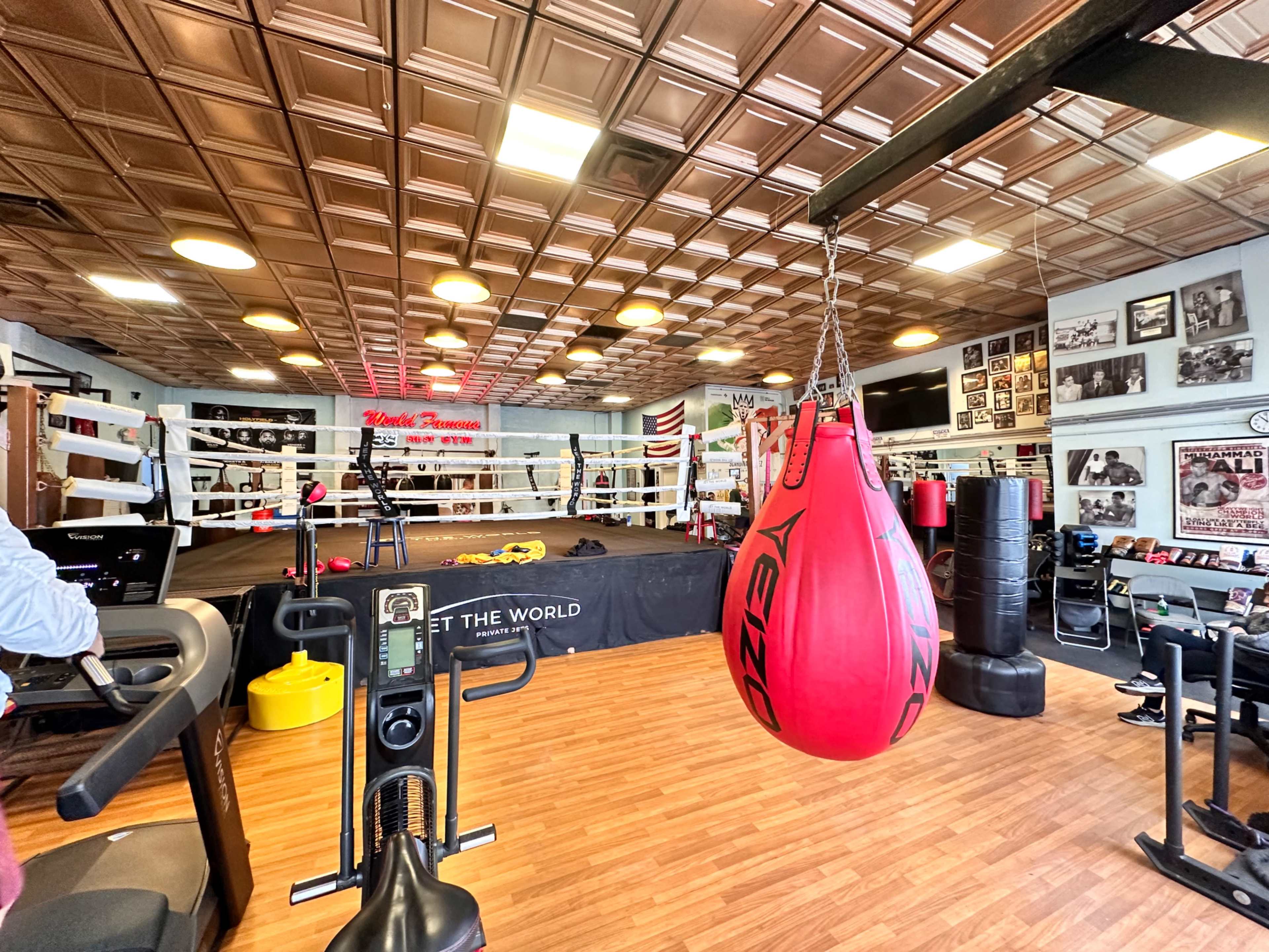 A boxing gym featuring a ring, exercise equipment, and colorful wall decorations, including photographs and a sign.