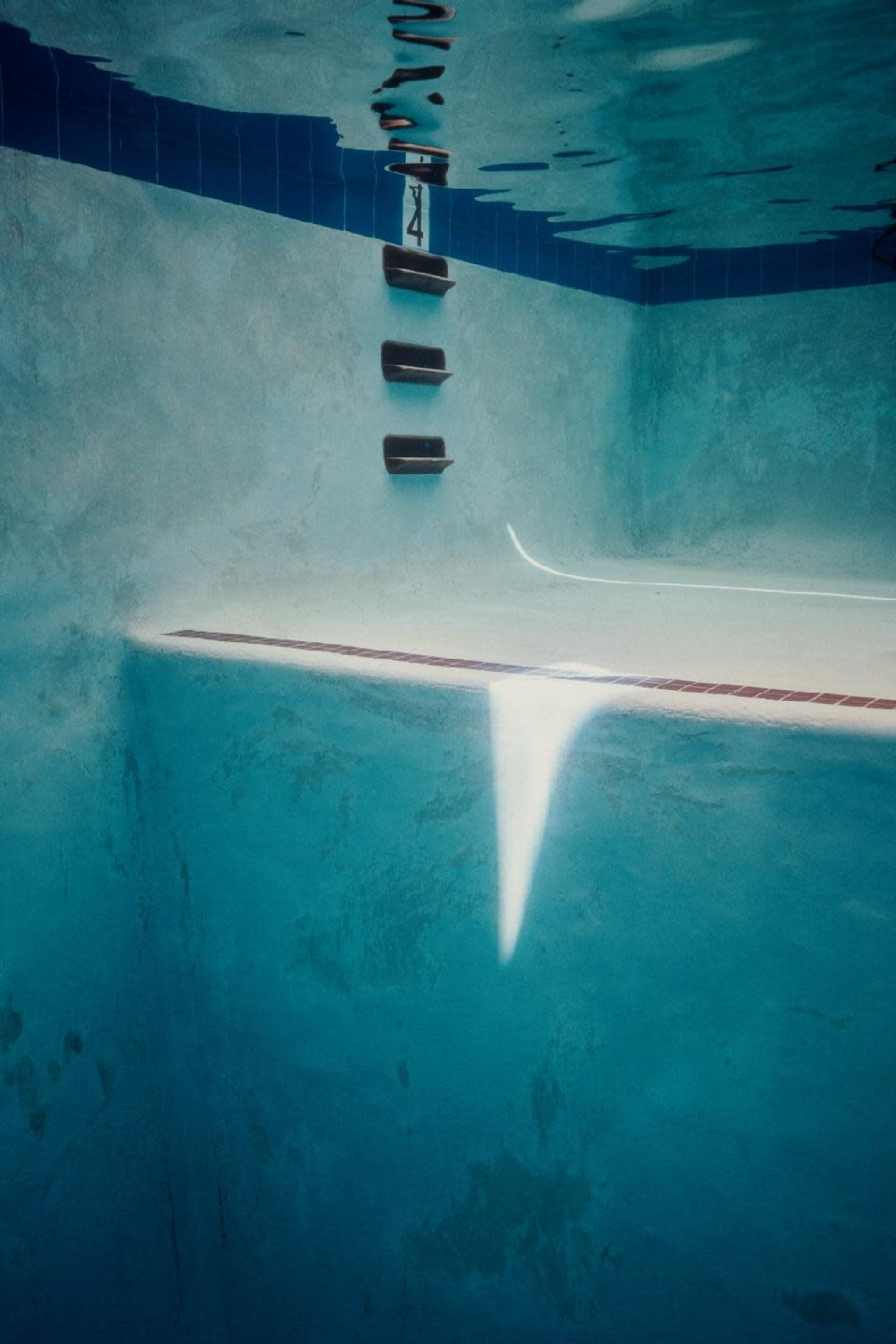 The interior of a swimming pool with a tiled ledge and a series of steps leading to the surface.