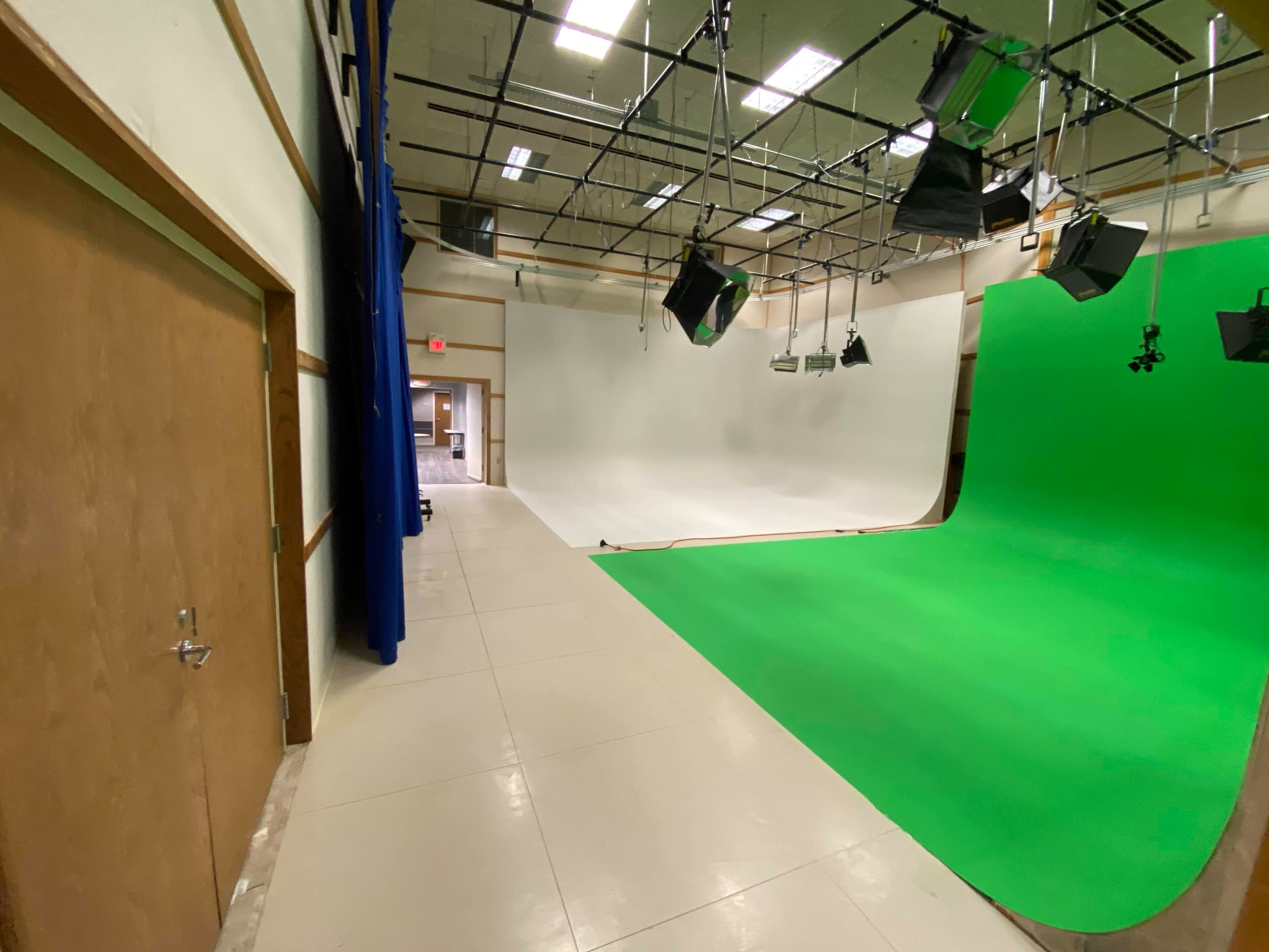 A production studio with a white backdrop and a green screen, along with overhead lighting and a door on the left.