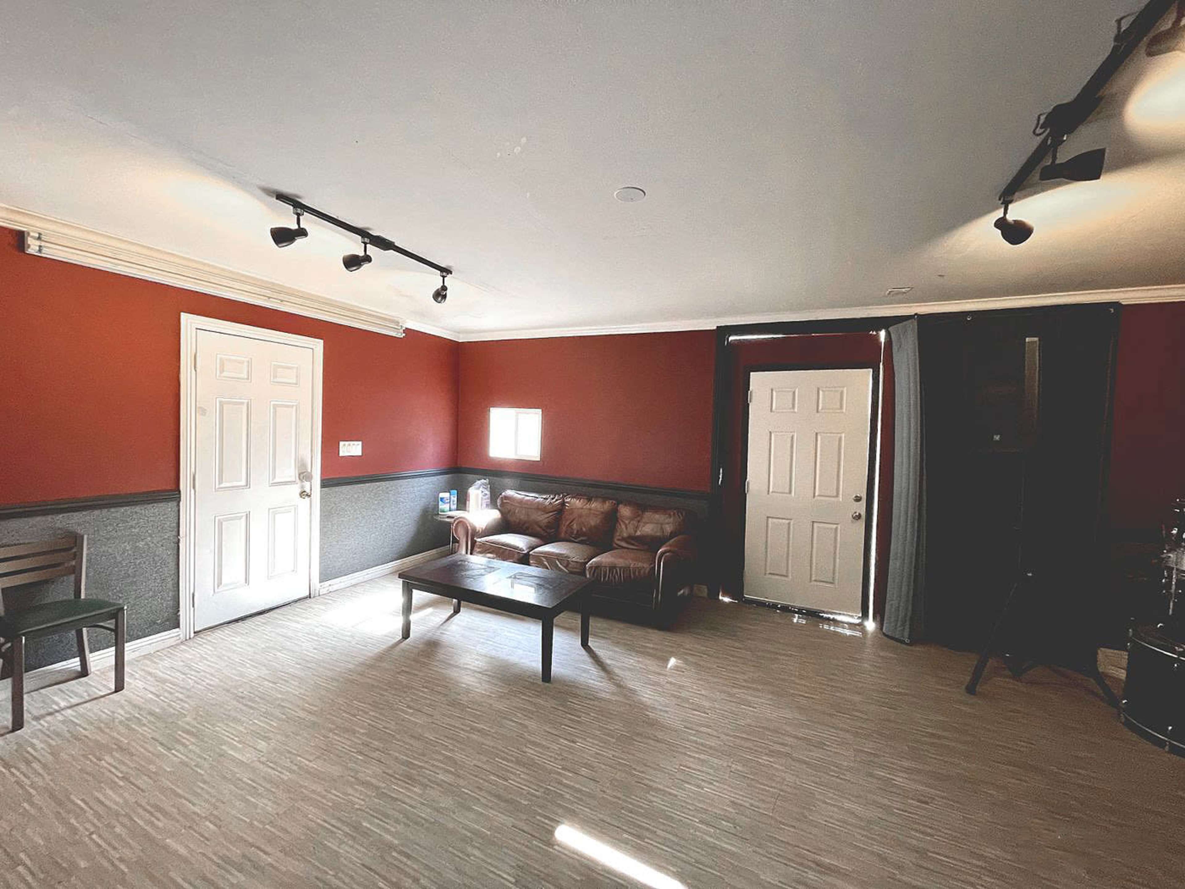 The image shows a sparsely furnished room with red walls, a brown leather couch, a coffee table, and two doors leading outside.