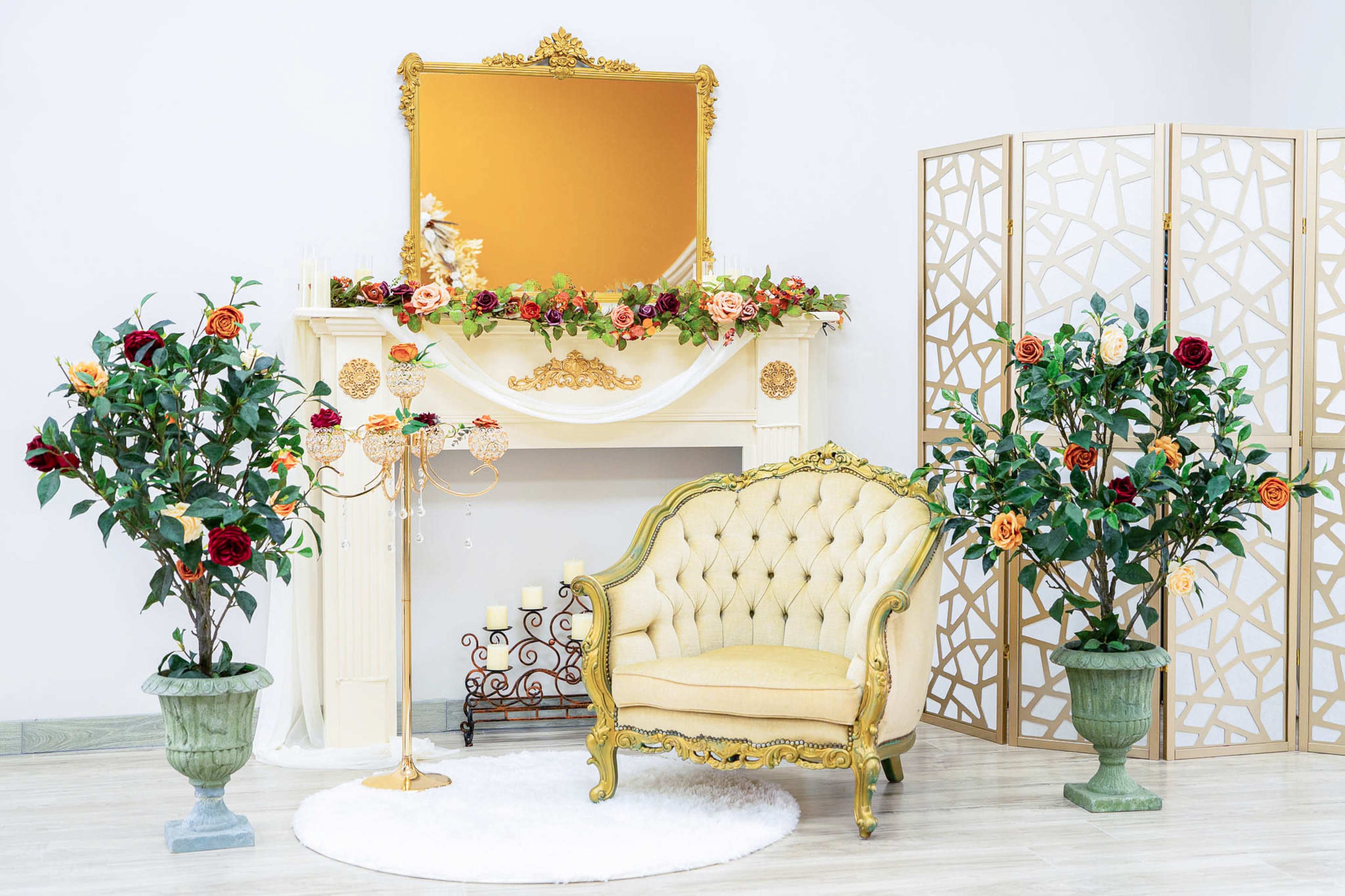 The image displays a styled interior scene featuring a golden-accented chair, a decorative fireplace with a mirror above it, and ornamental plants on either side.