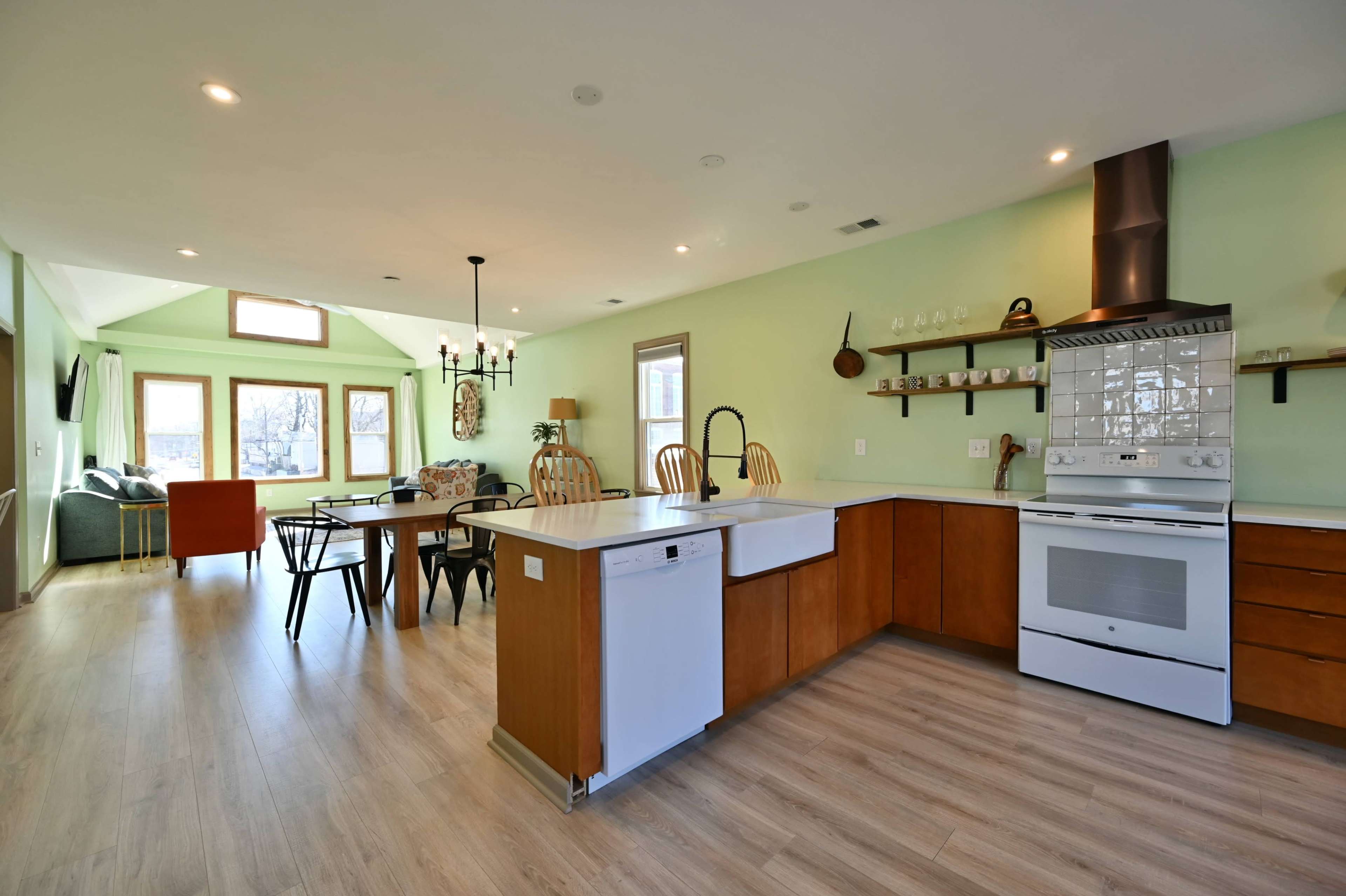The image shows a modern kitchen and dining area with a central island, wooden cabinets, and a dining table surrounded by various chairs.