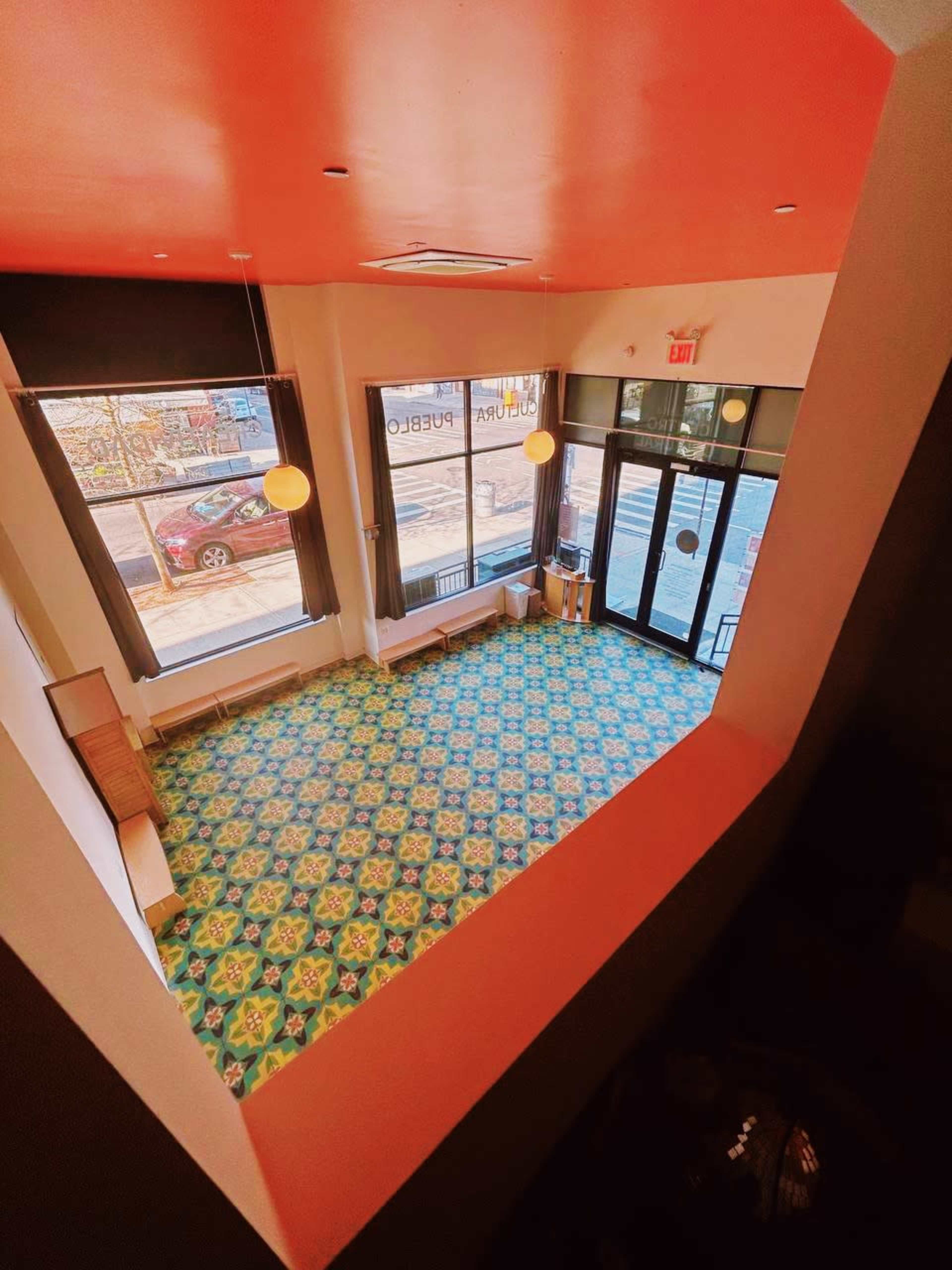 A spacious room with colorful tiled flooring, large windows, and a bright orange ceiling.