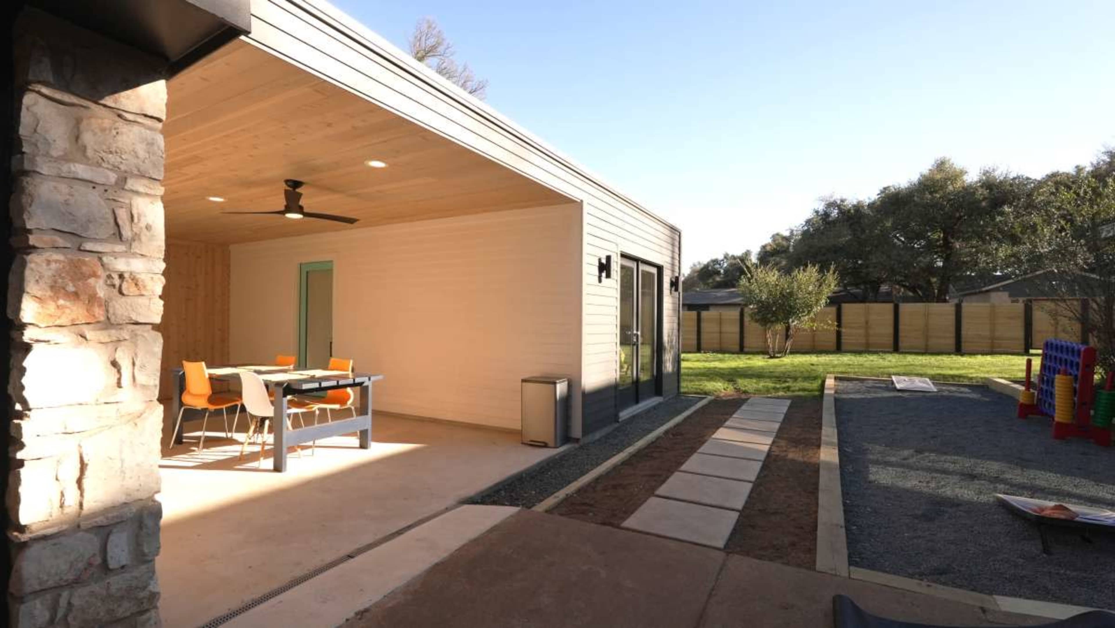 The image shows a modern building exterior leading to an outdoor space with a dining table and playground equipment in the background.