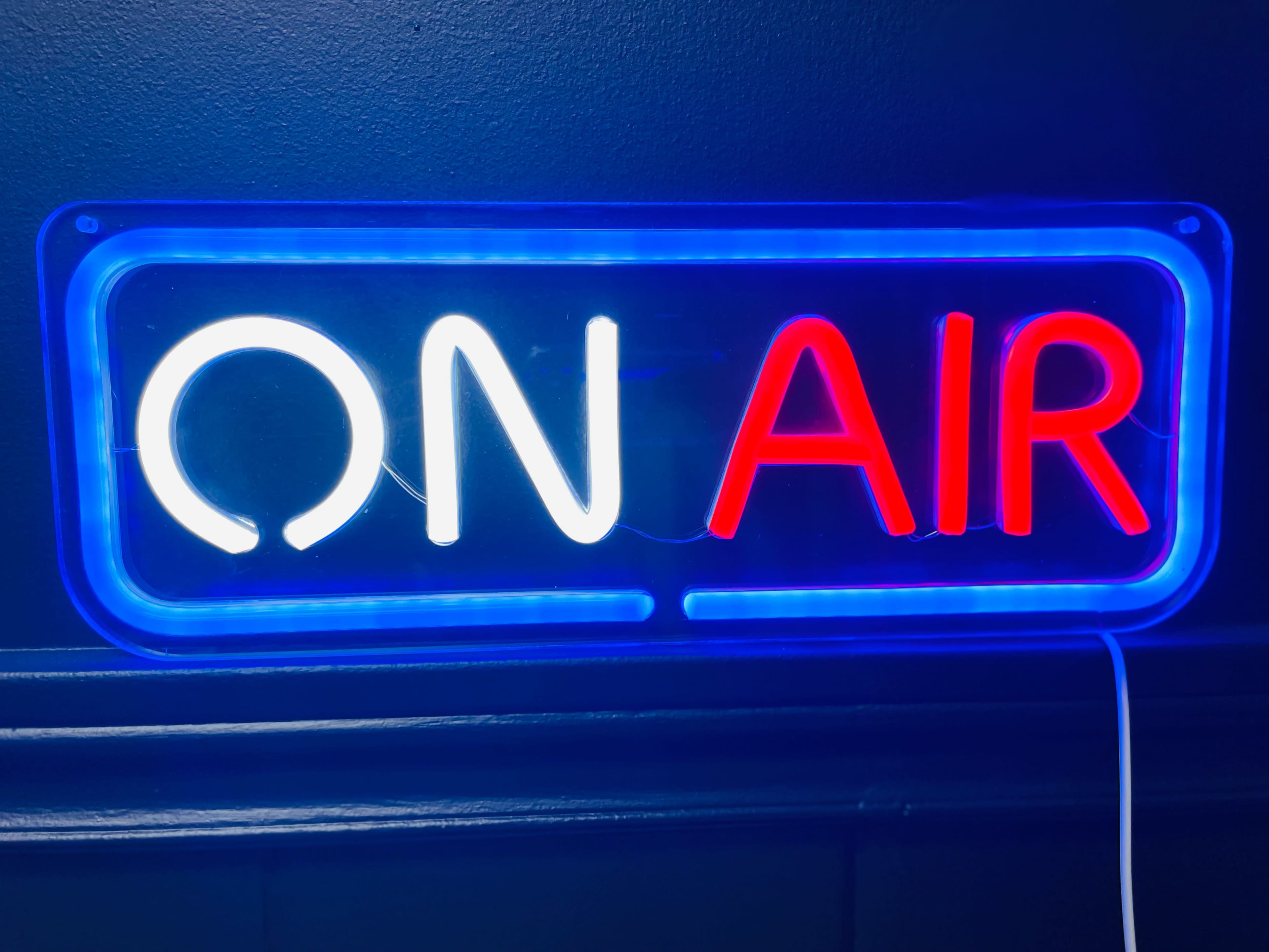 A neon sign displays the words "ON AIR" in white and red letters against a dark background.