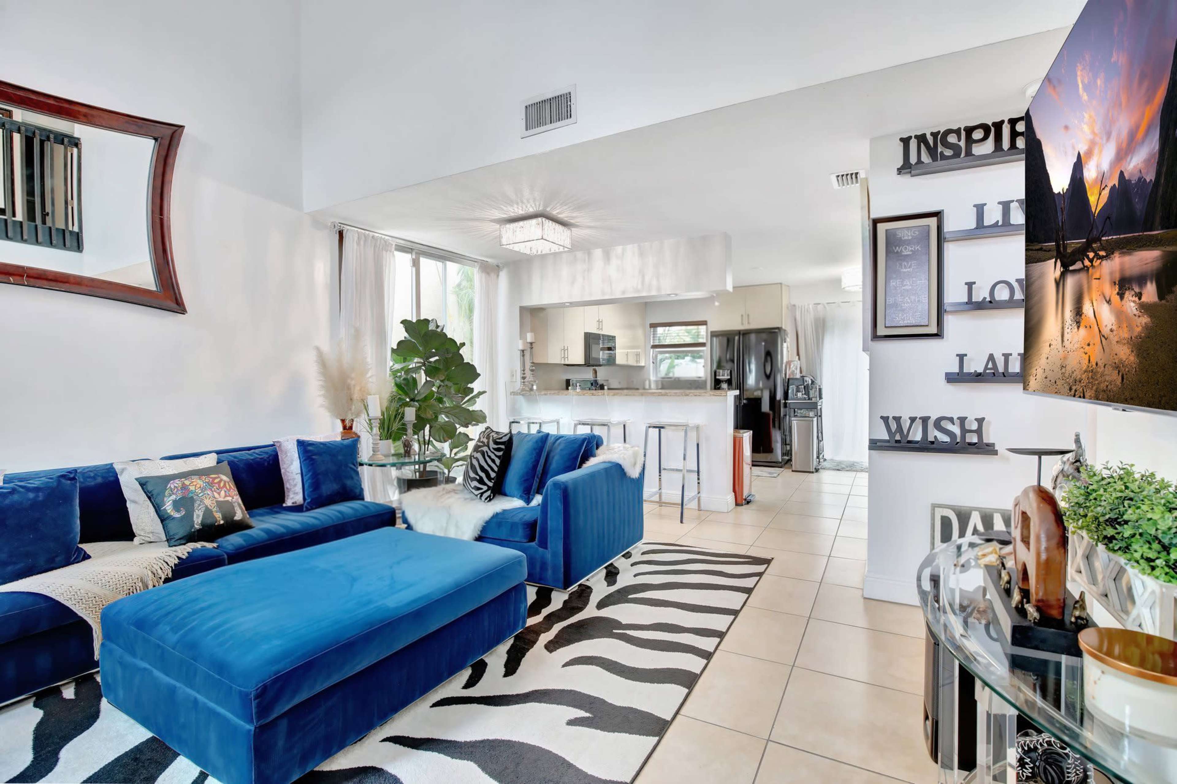 The living area features a blue sectional sofa, a zebra-striped rug, and a kitchen area visible in the background with bar seating.