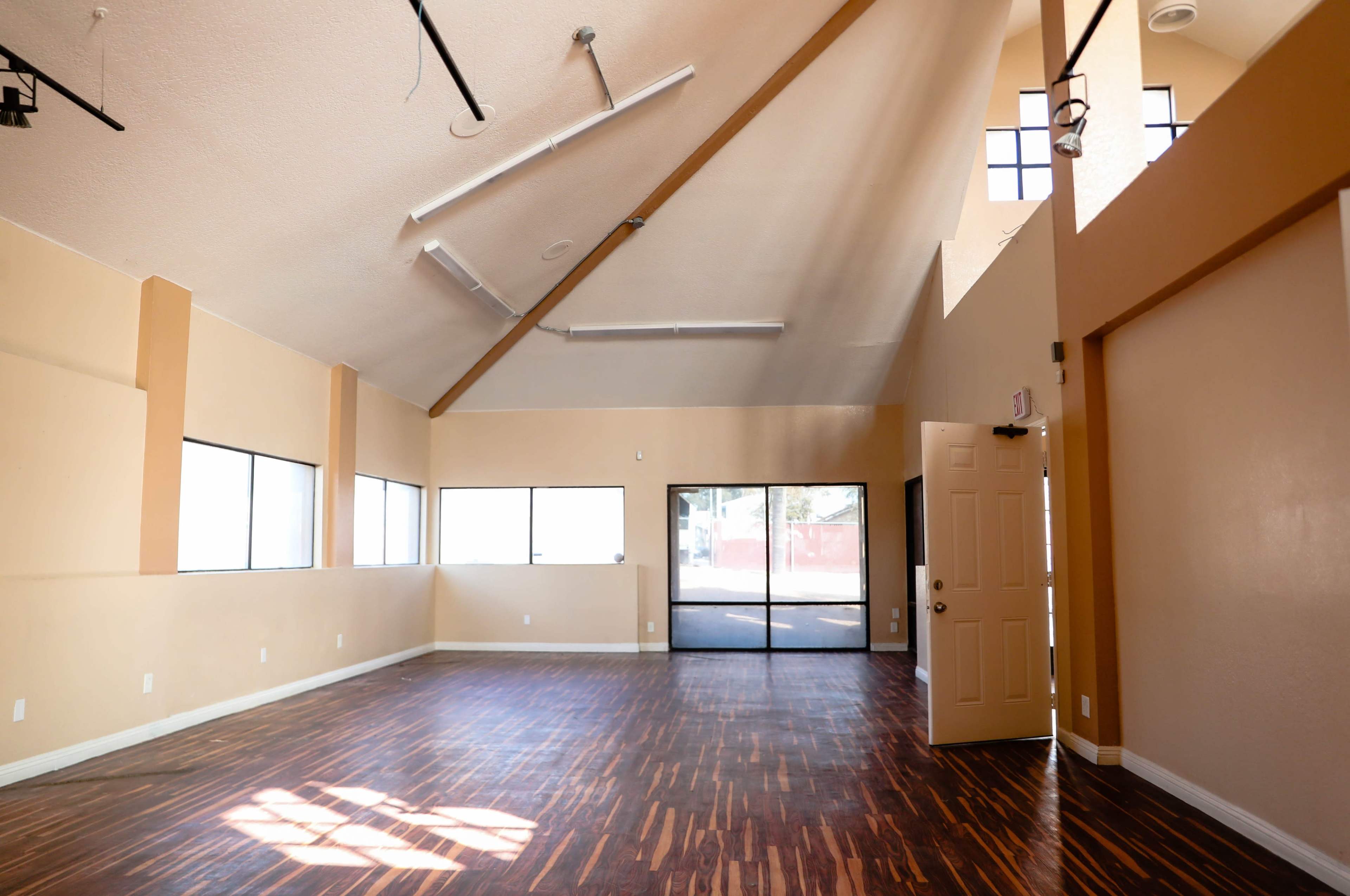 An empty room with high ceilings, large windows, and hardwood flooring.
