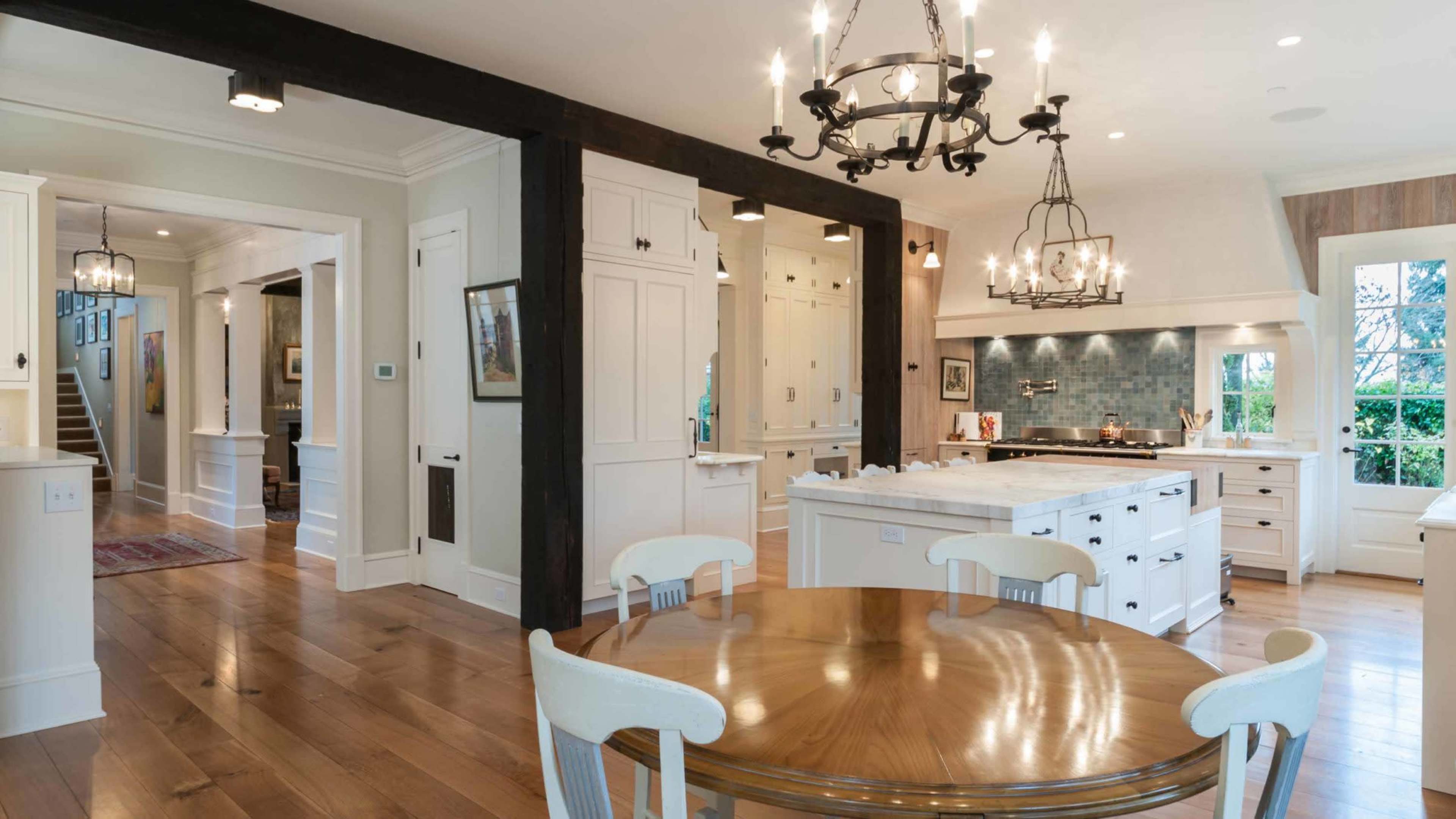 A modern kitchen featuring white cabinets, a large island with a marble countertop, and a round wooden dining table illuminated by a chandelier.