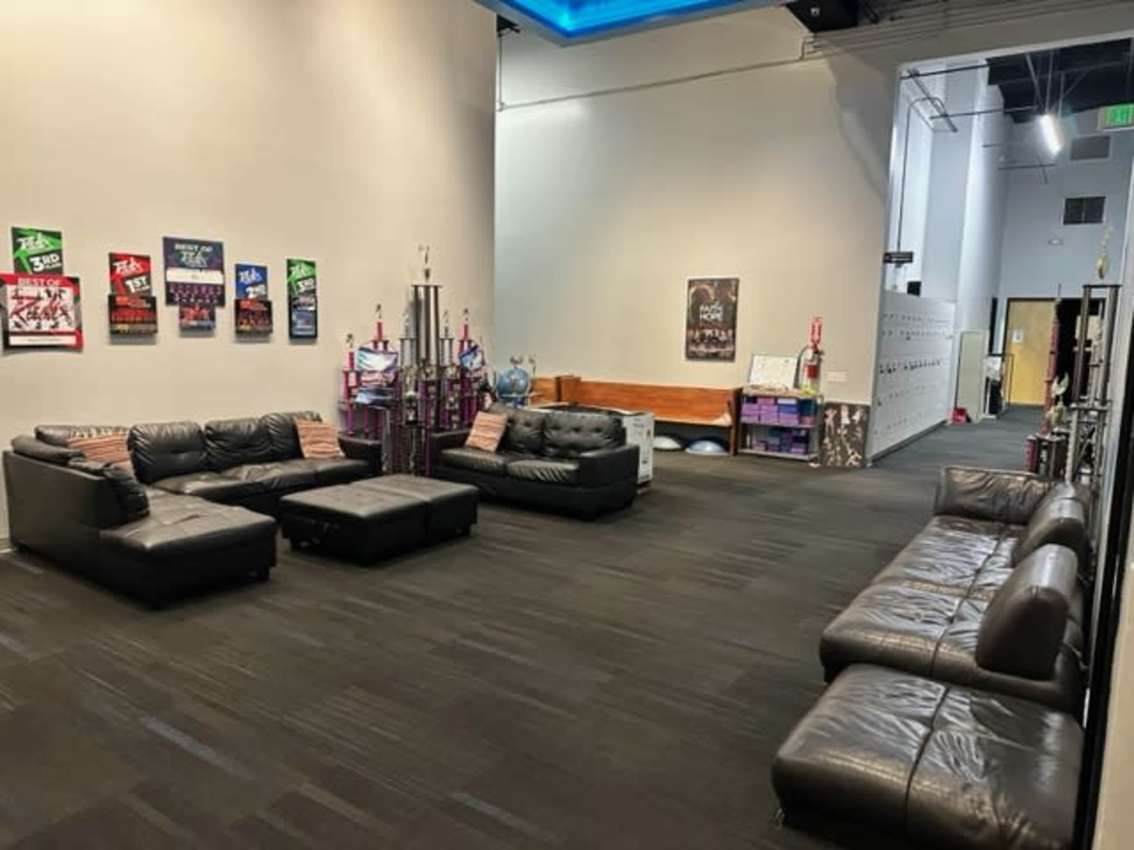 A spacious lounge area with black leather couches, a trophy display, and posters on the walls.