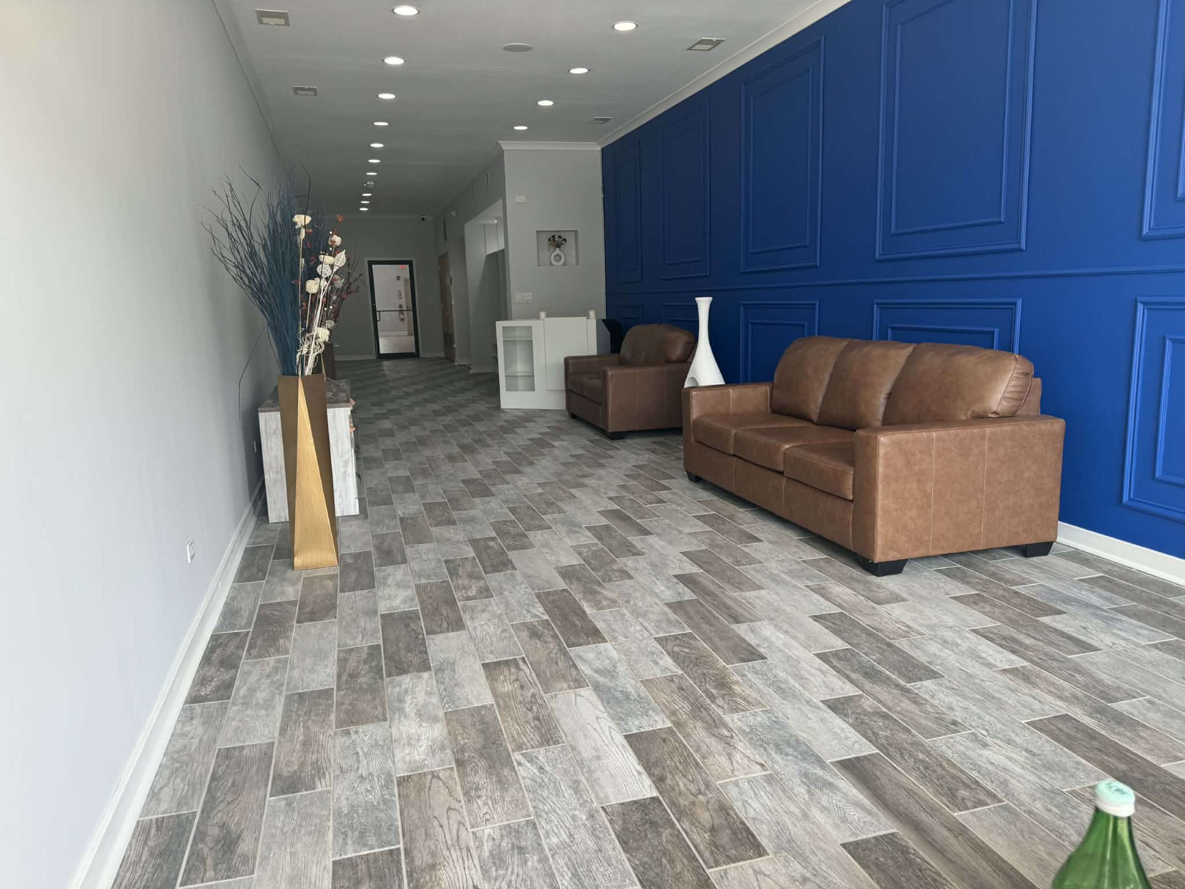 The image shows a spacious room with a blue accent wall, two brown sofas, and a patterned tile floor.