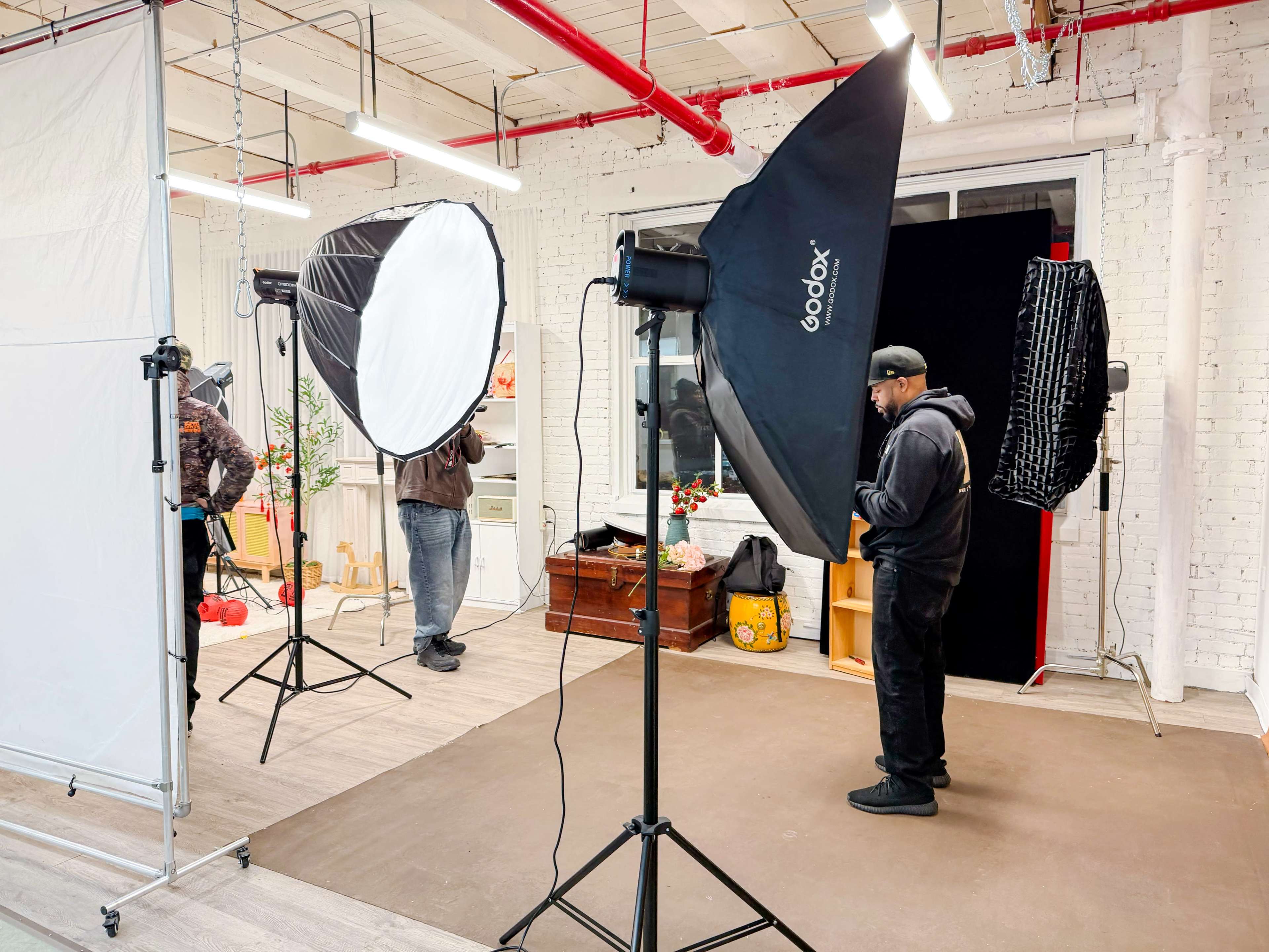 A photography studio is set up with multiple lighting equipment and backdrops, with individuals preparing for a photo shoot.