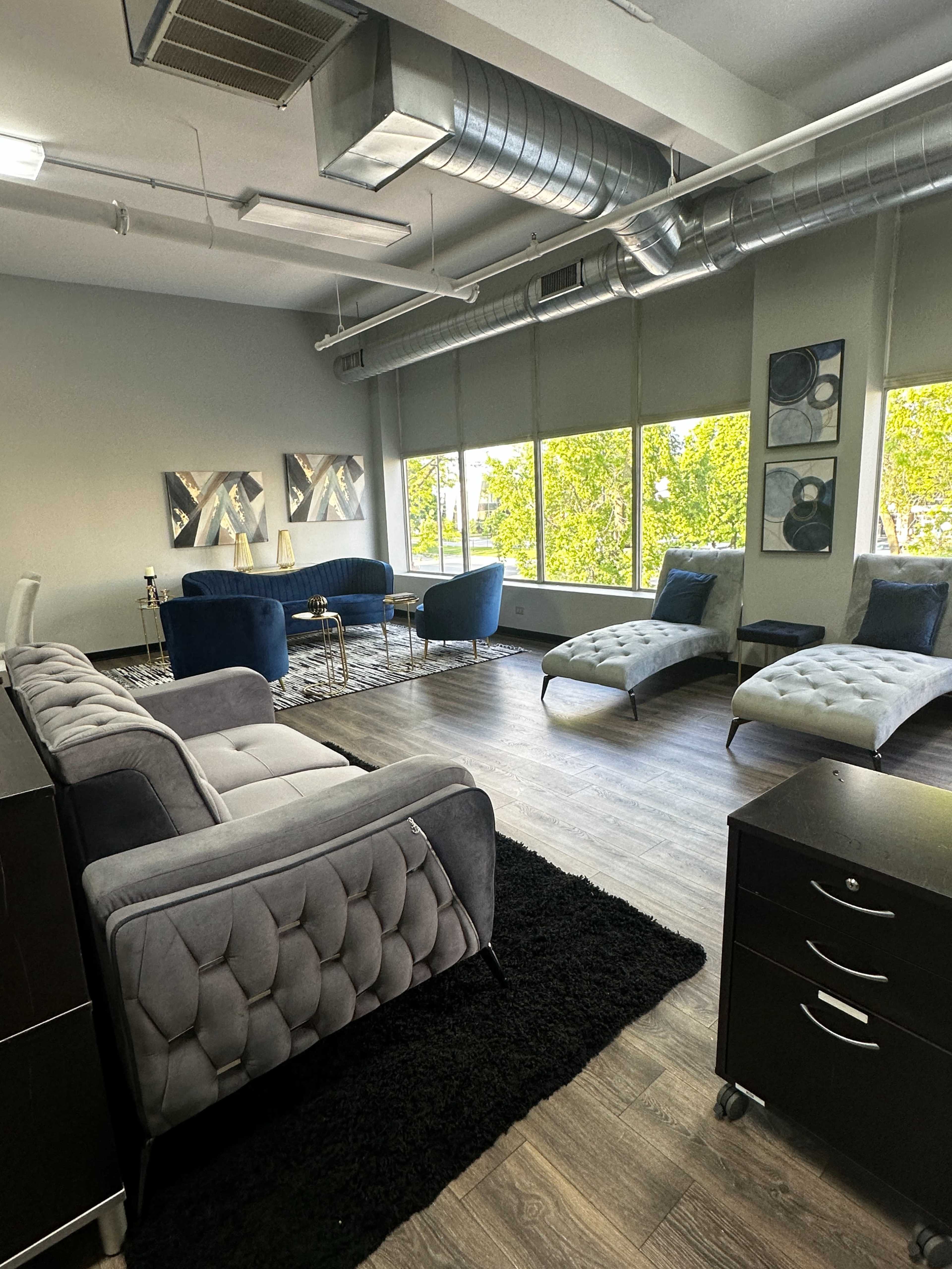 A modern office space features gray and blue furniture with large windows that allow natural light to illuminate the room.