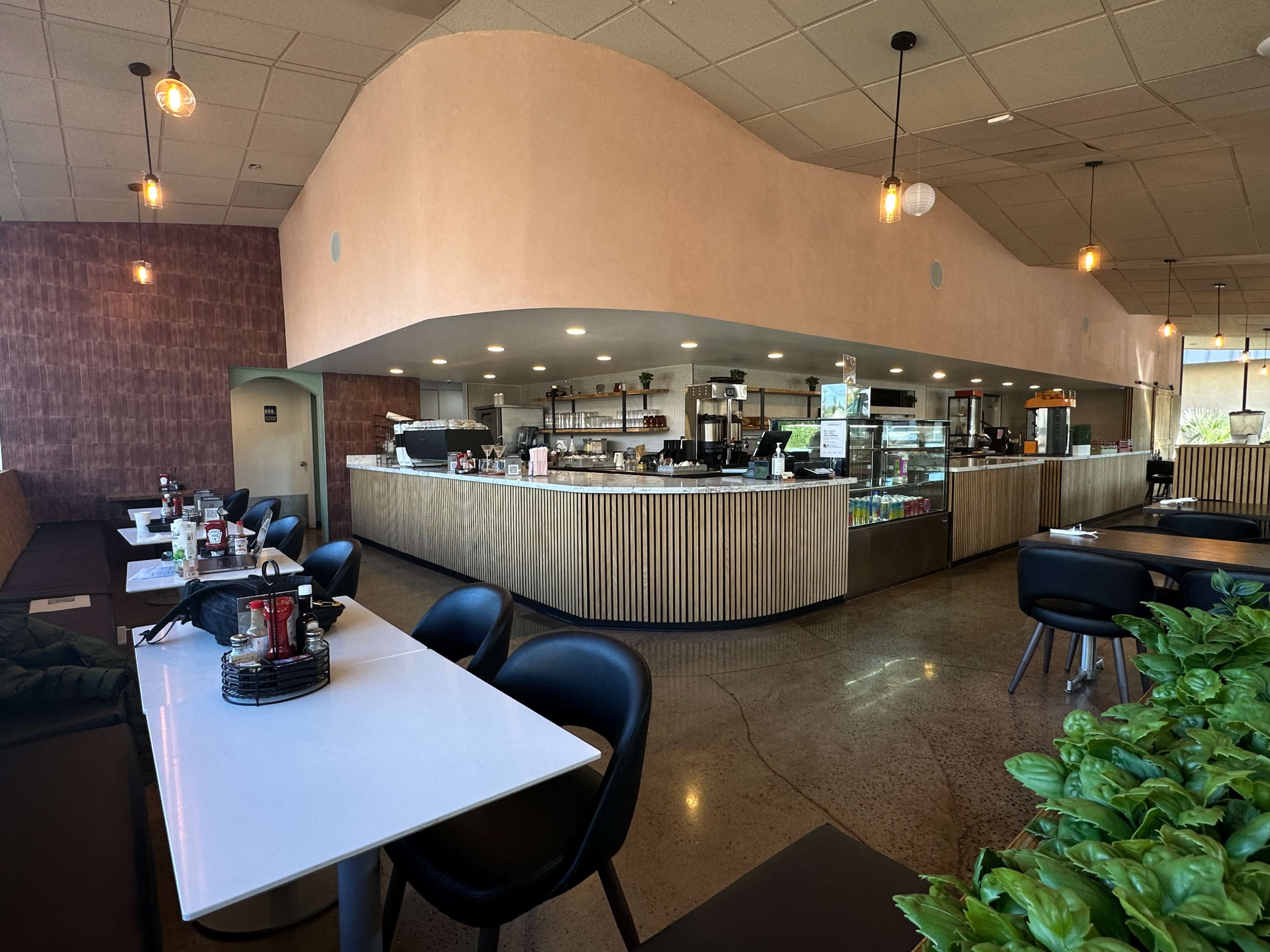 The image shows a modern café interior with a curved counter, seating arrangements, and large windows allowing natural light to enter.