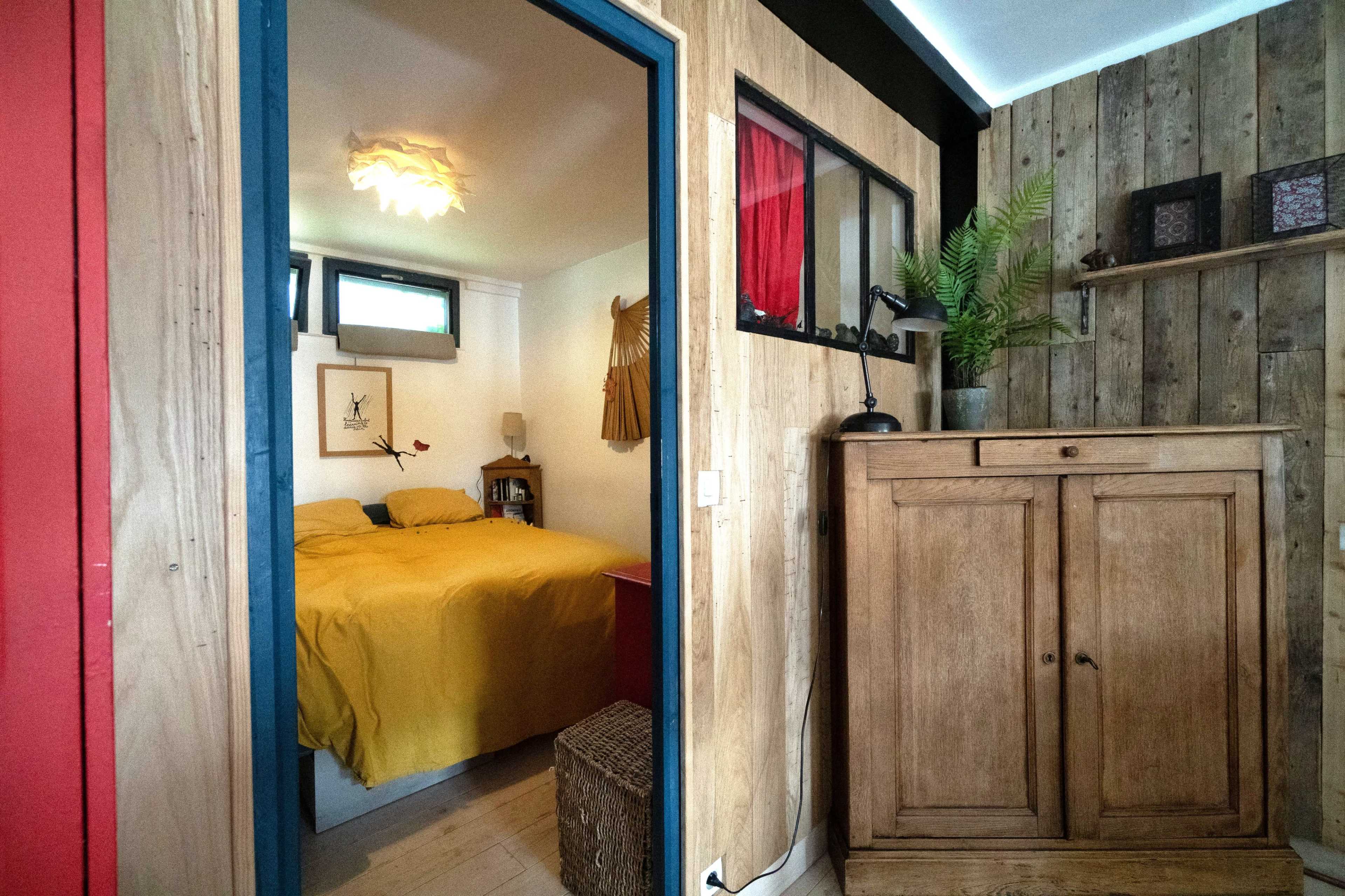 A compact room with a yellow bedspread, wooden furniture, and a small window, viewed through an open doorway.